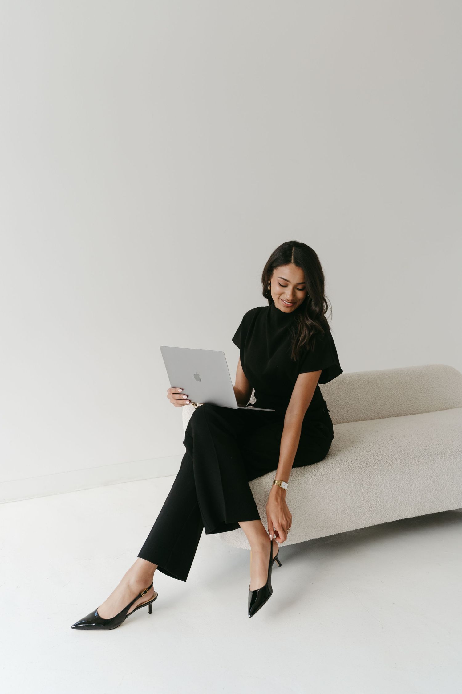 Professional sitting on white couch with laptop in modern minimal setting.