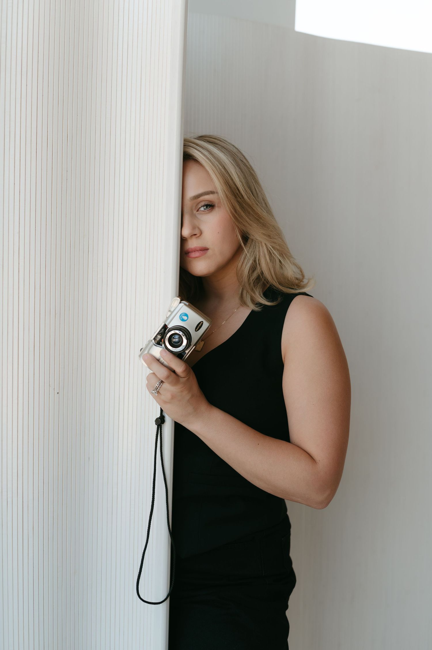 Artistic portrait with vintage camera against white textured wall.