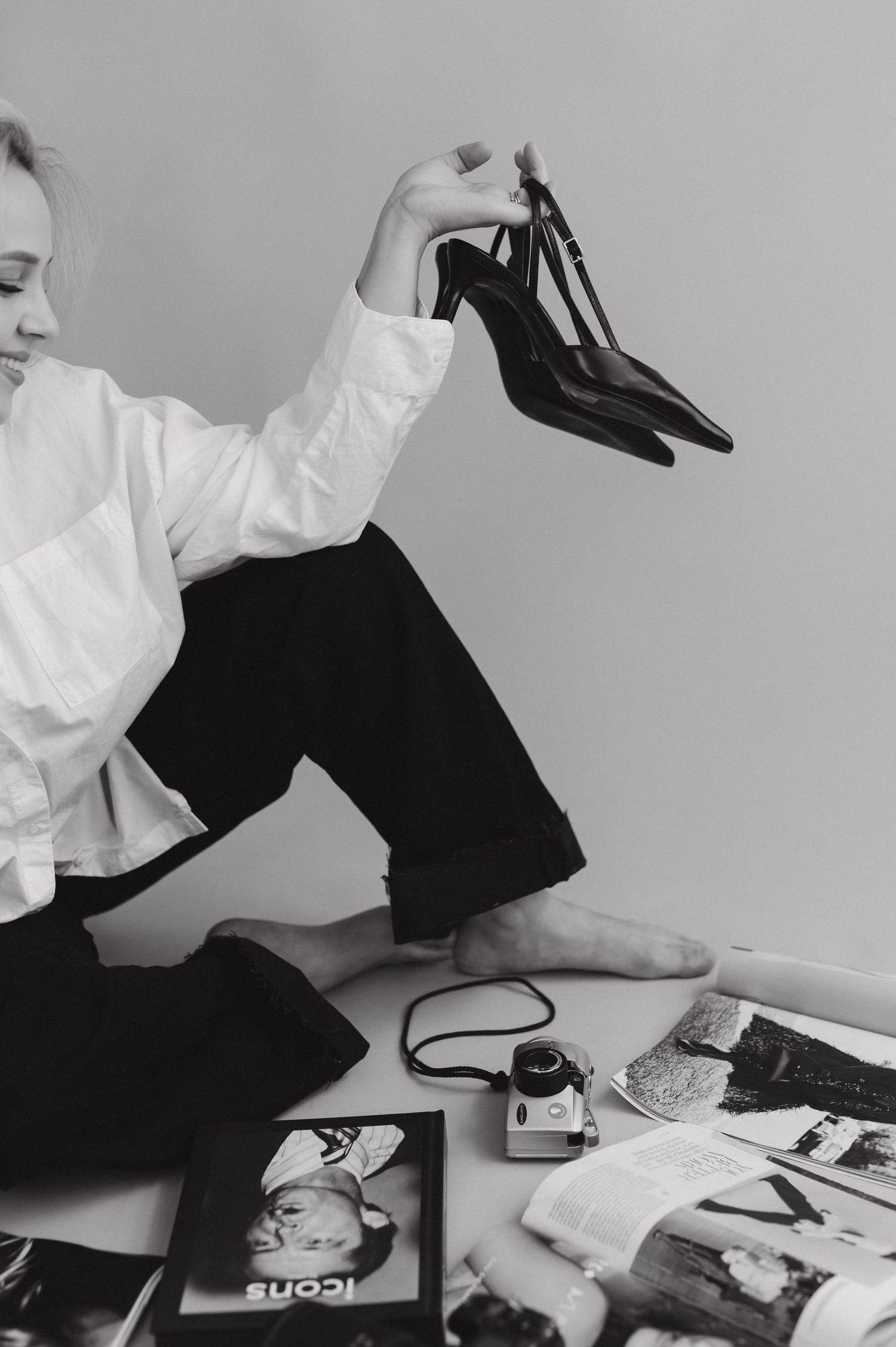 Person arranging black stiletto heels among fashion magazines and photography equipment.