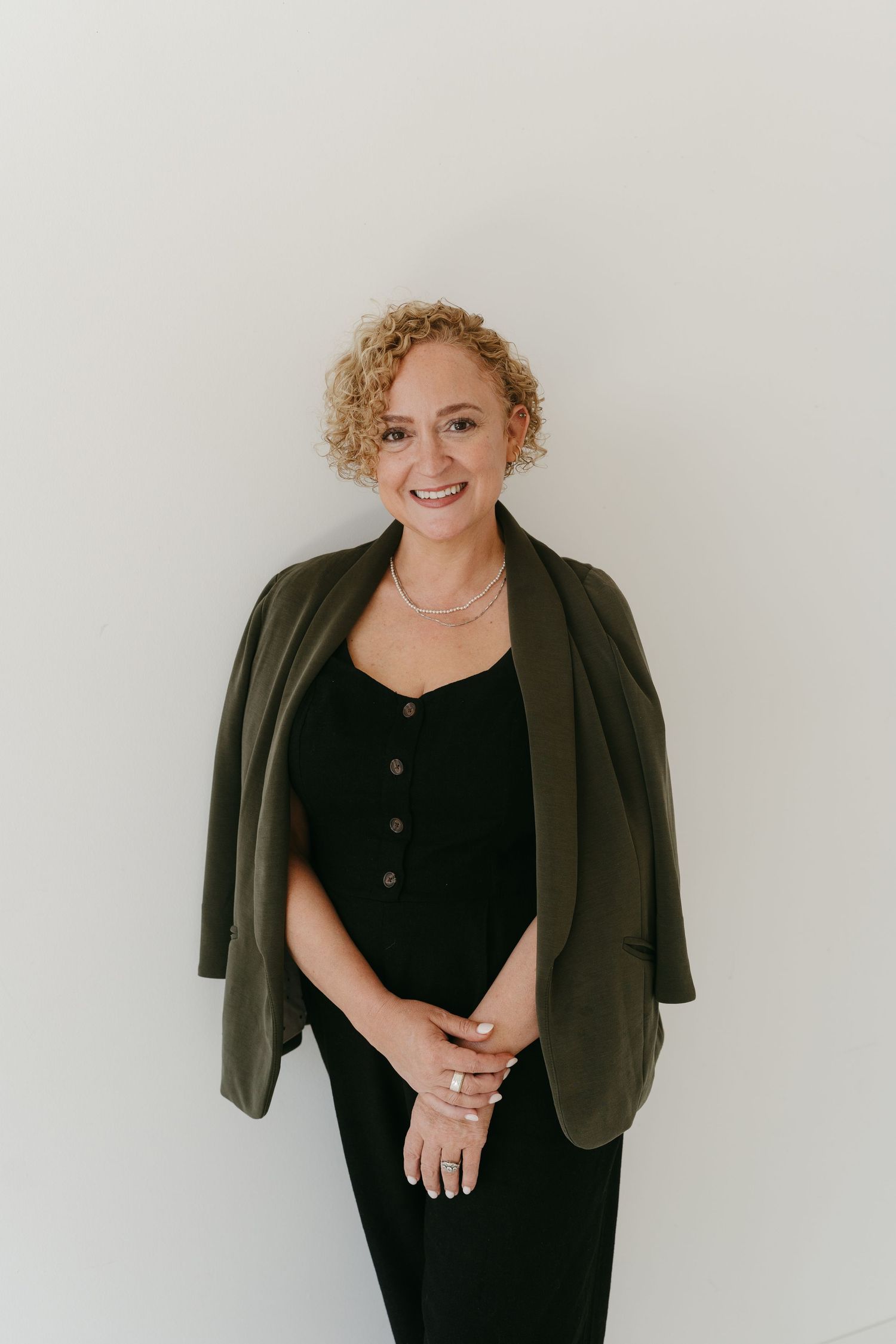 Person wearing black outfit and blazer posing against white background.