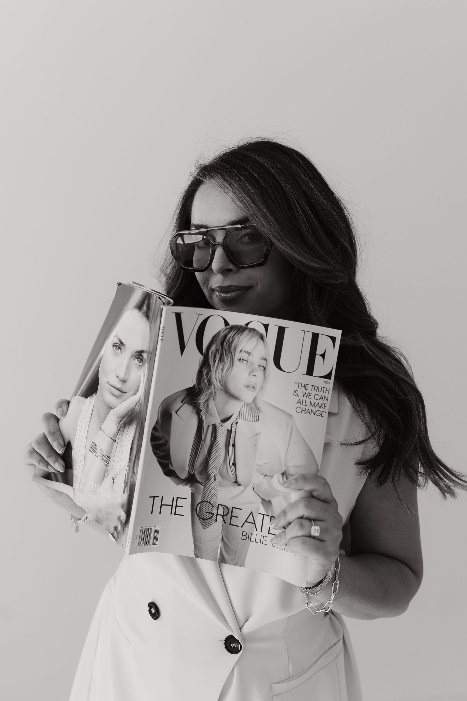A stylish figure in white holds fashion magazines against a light background.