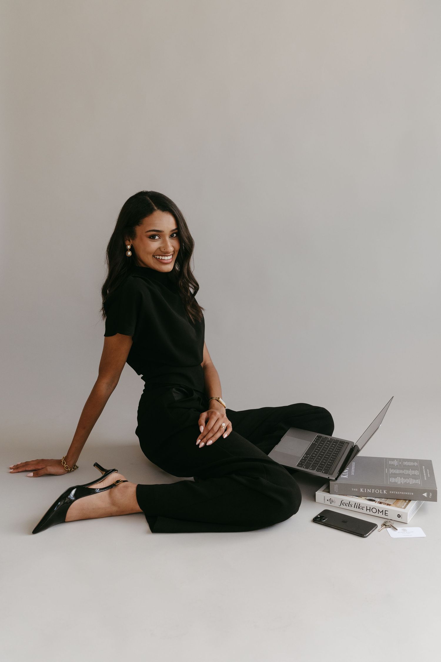 Casual business photoshoot with person in black outfit working on laptop on floor.