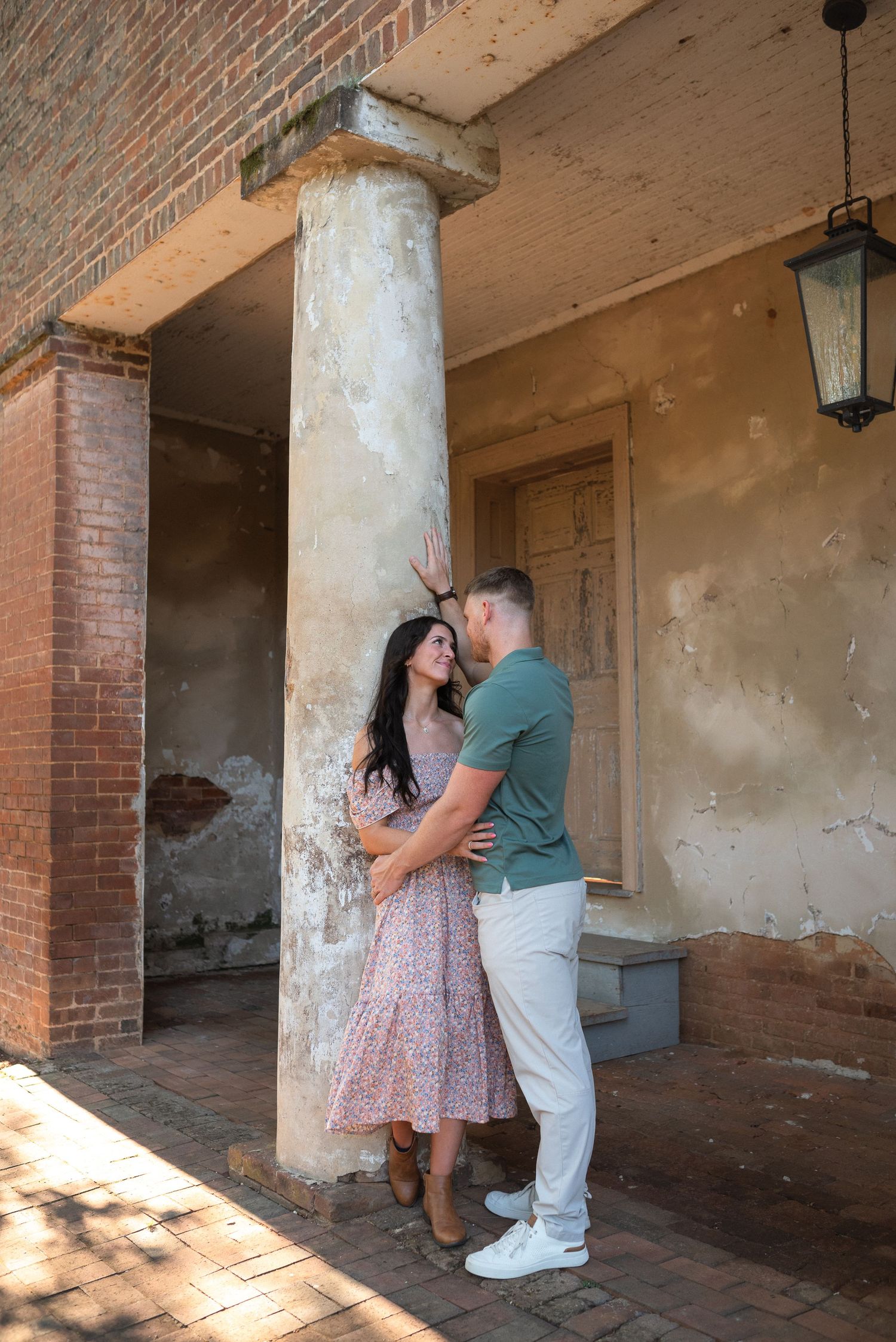 Couple sharing an intimate moment beside a rustic column on a historic brick building.