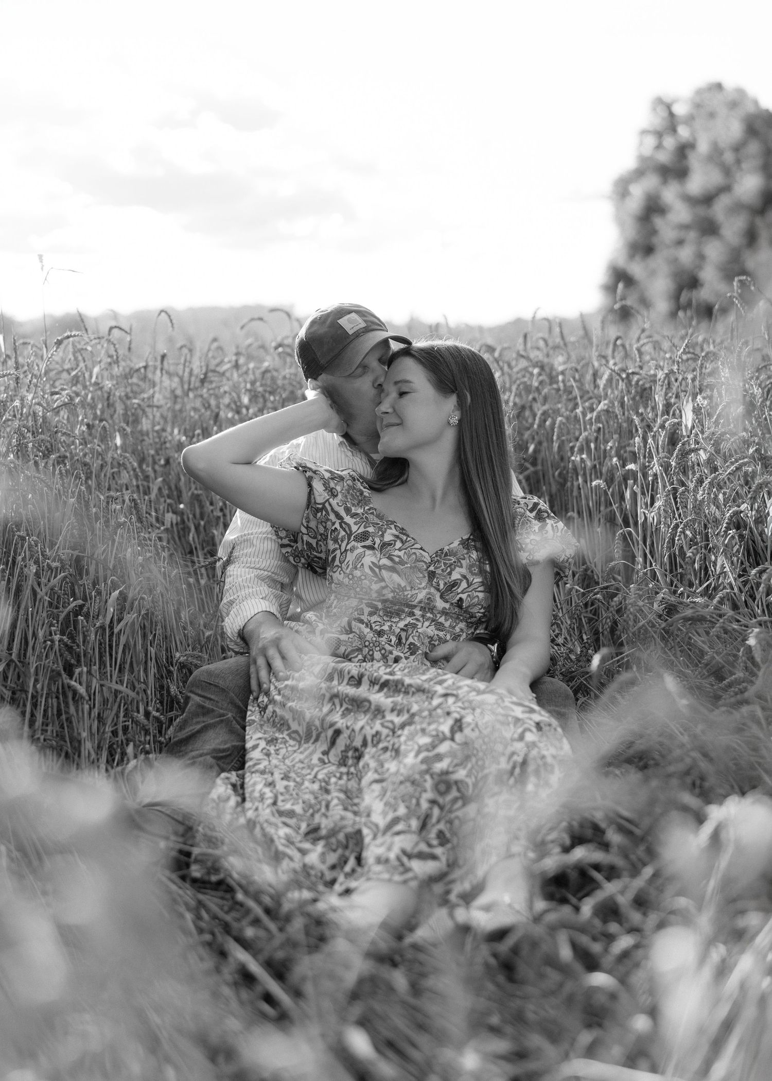 Black and white photo of a romantic couple sitting together in a wheat field, sharing an intimate moment.