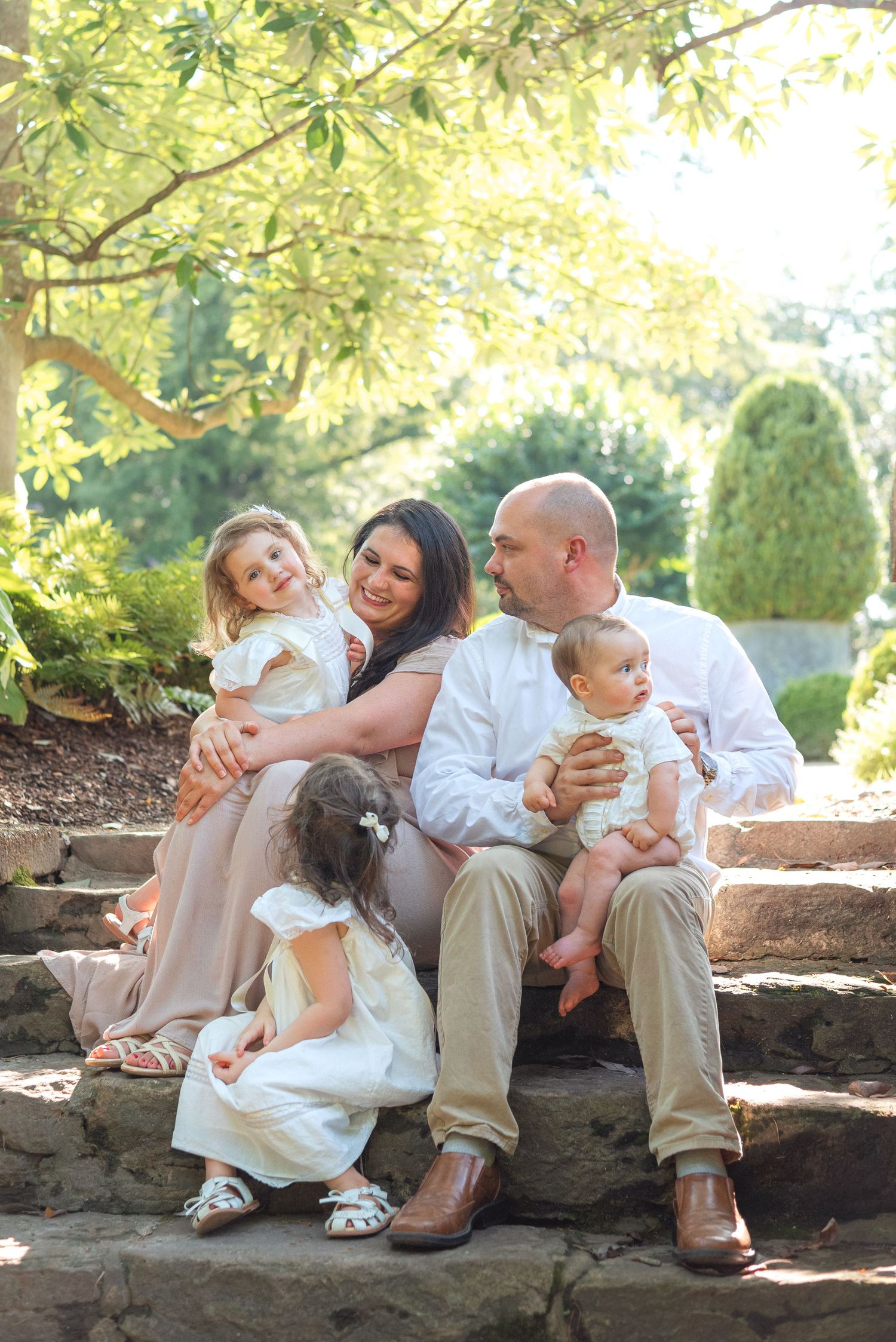 Happy family of five sharing a joyful moment on stone garden steps, parents smiling at each other with three young children.