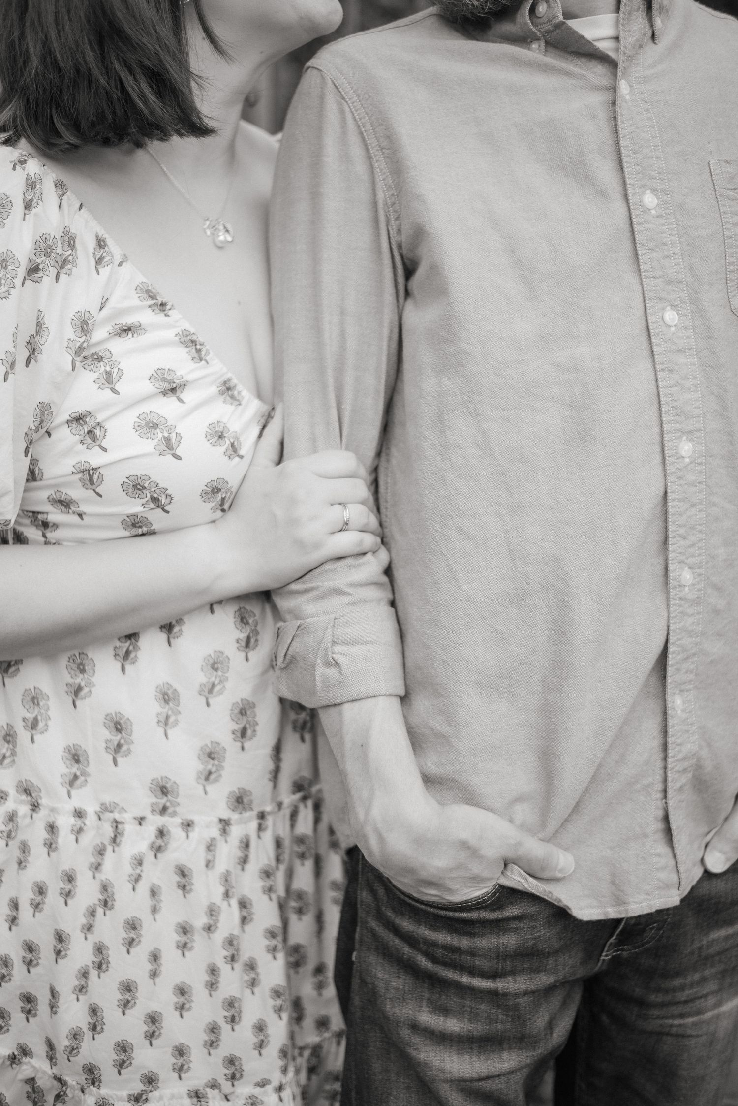 Black and white close-up of couple holding hands, woman in floral dress leaning on mans arm.