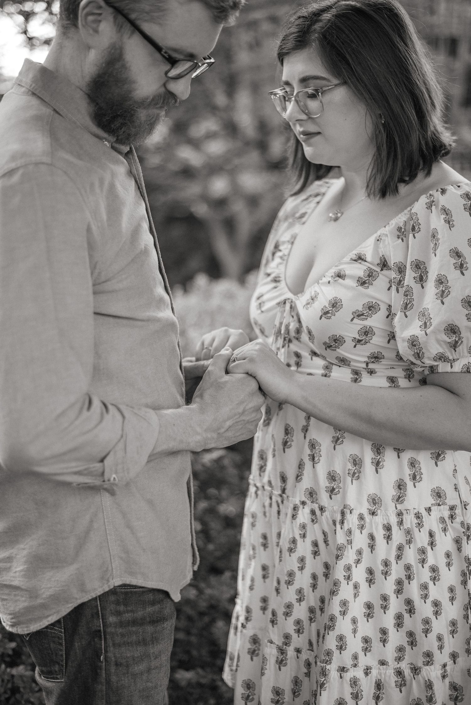 Black and white photo of a couple holding hands and looking down together outdoors.