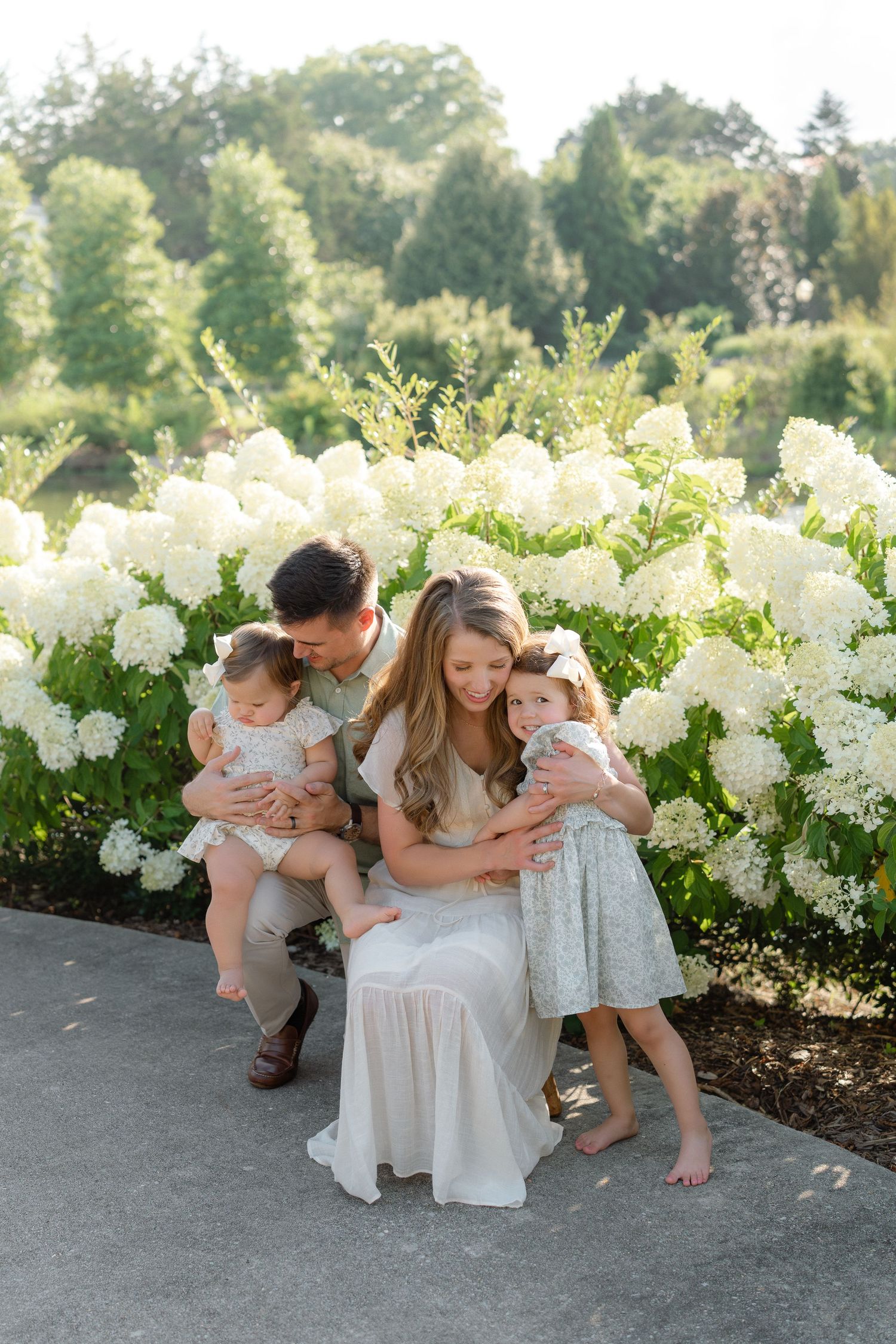Family of four posing in front of white hydrangea bushes in a lush garden setting.