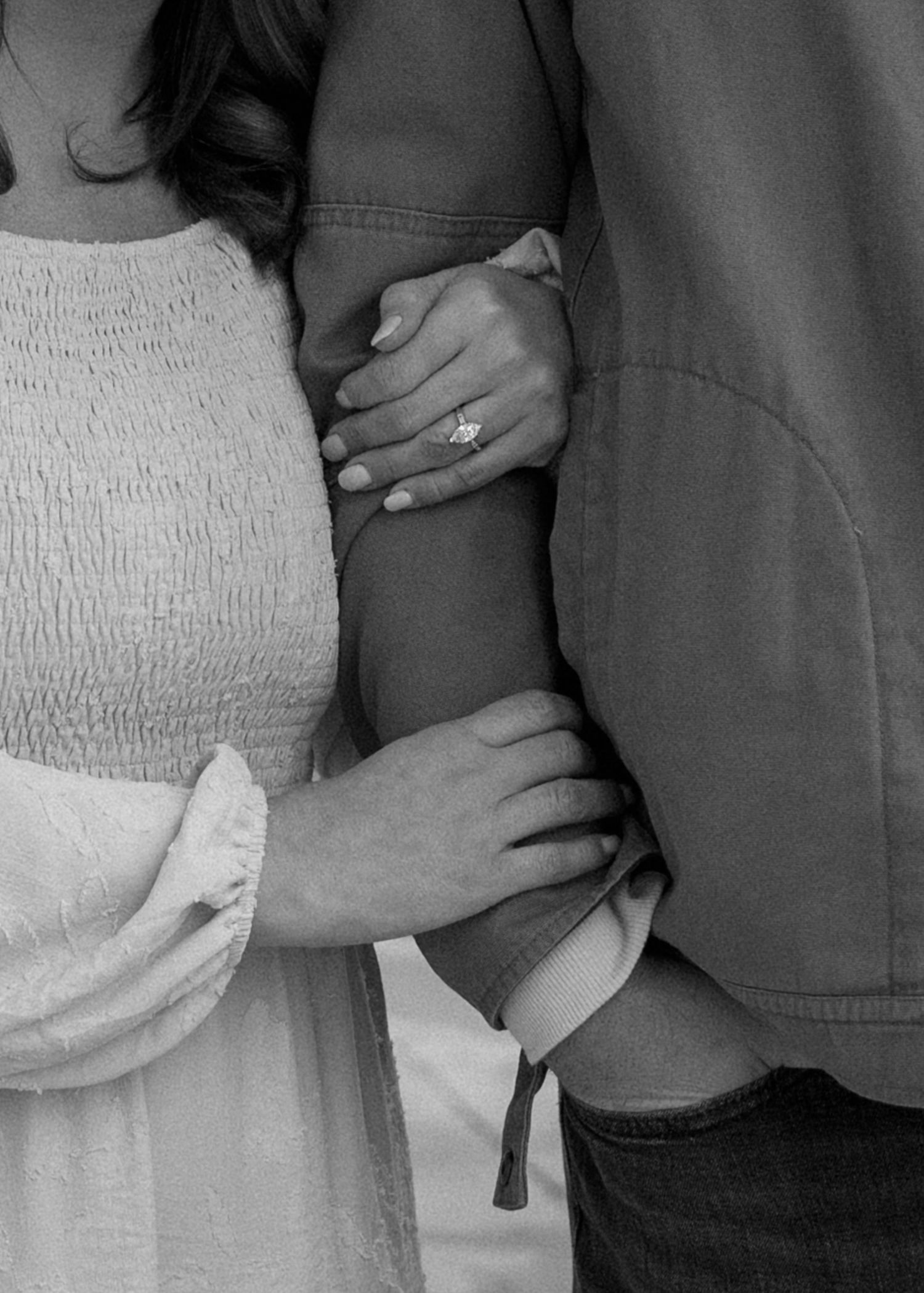 Black and white close-up of engaged couple holding arms, showcasing a sparkling diamond engagement ring.