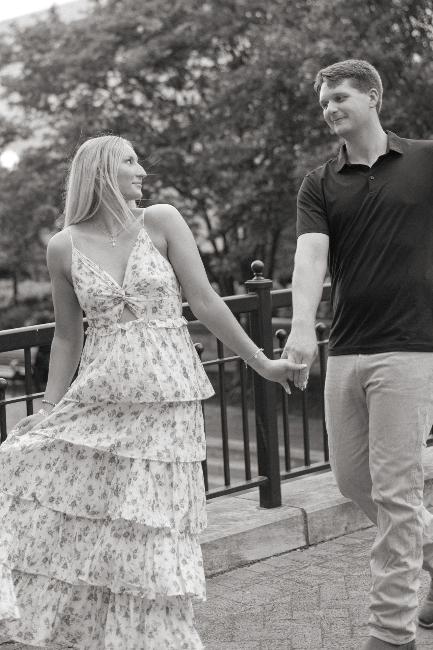 Black and white photo of a couple holding hands and smiling at each other on a brick path.