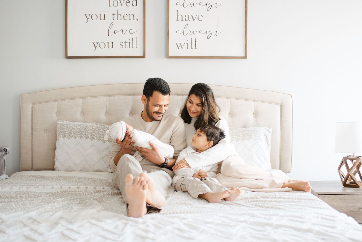 Happy family with newborn and toddler sitting together on a cozy white bed.