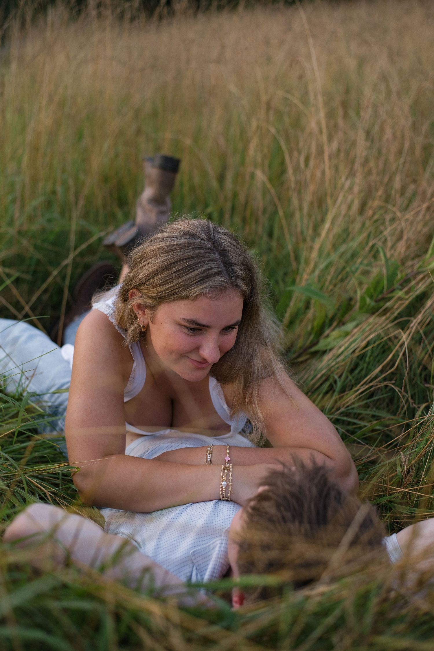 Woman smiling down at partner while lying together in tall golden grass at sunset.