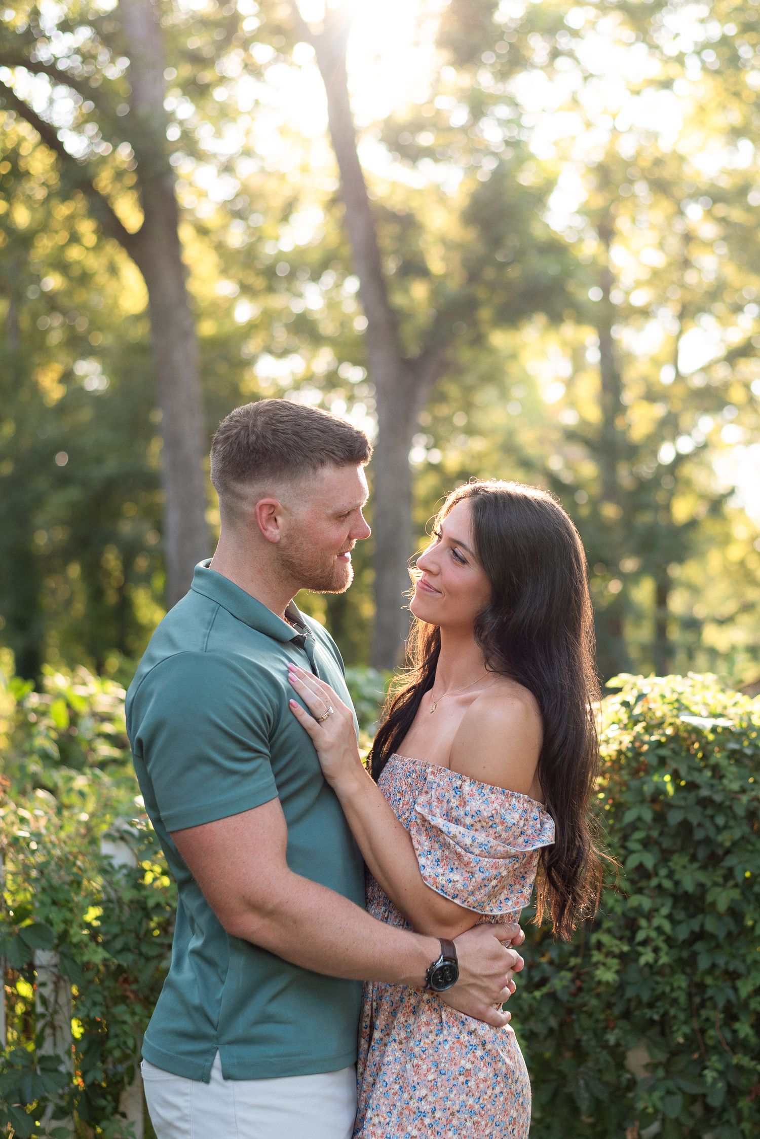 Couple embracing and gazing at each other in a sunlit green park during golden hour.