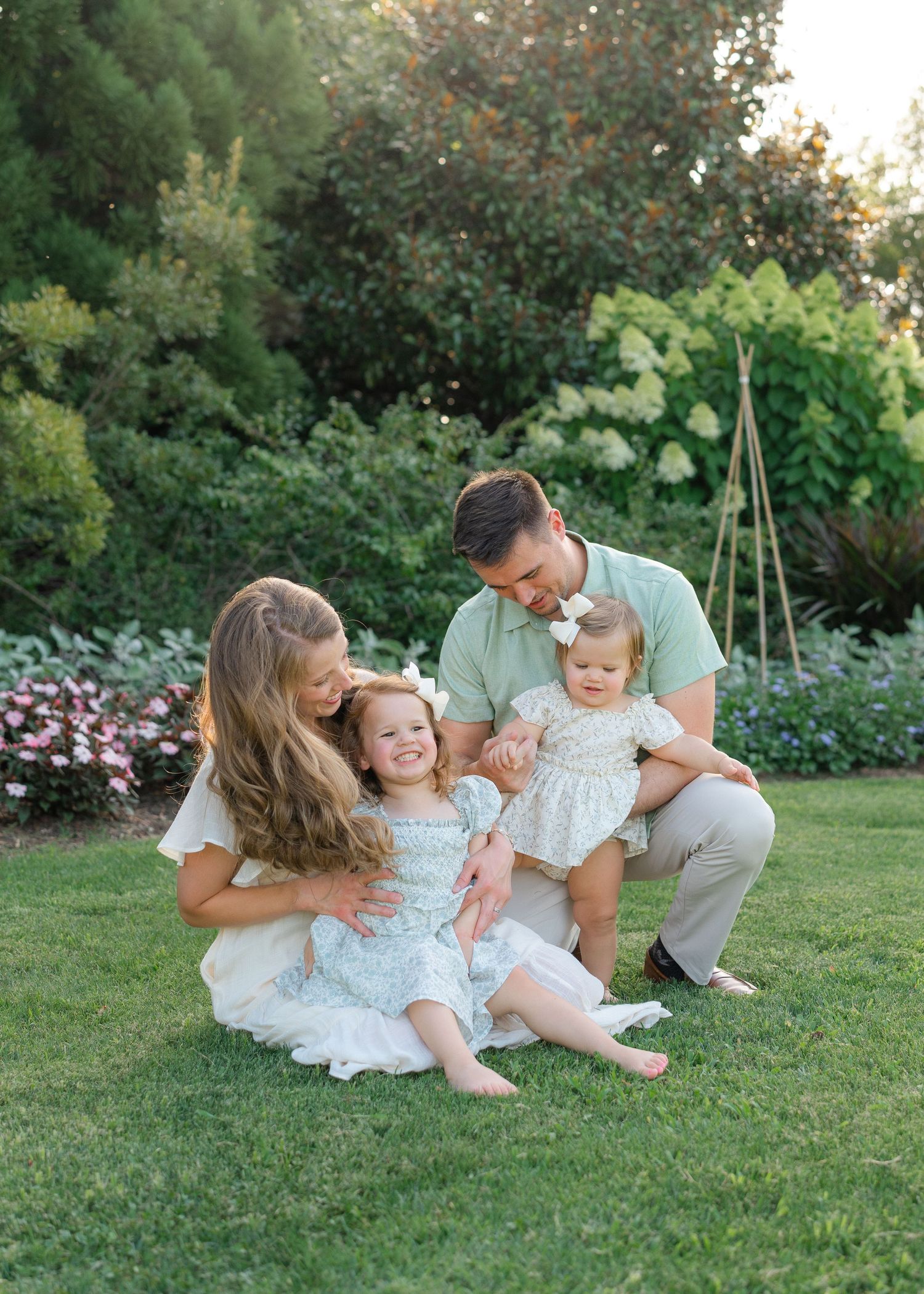 Happy family of four enjoying a sunny day together on green grass in a garden.