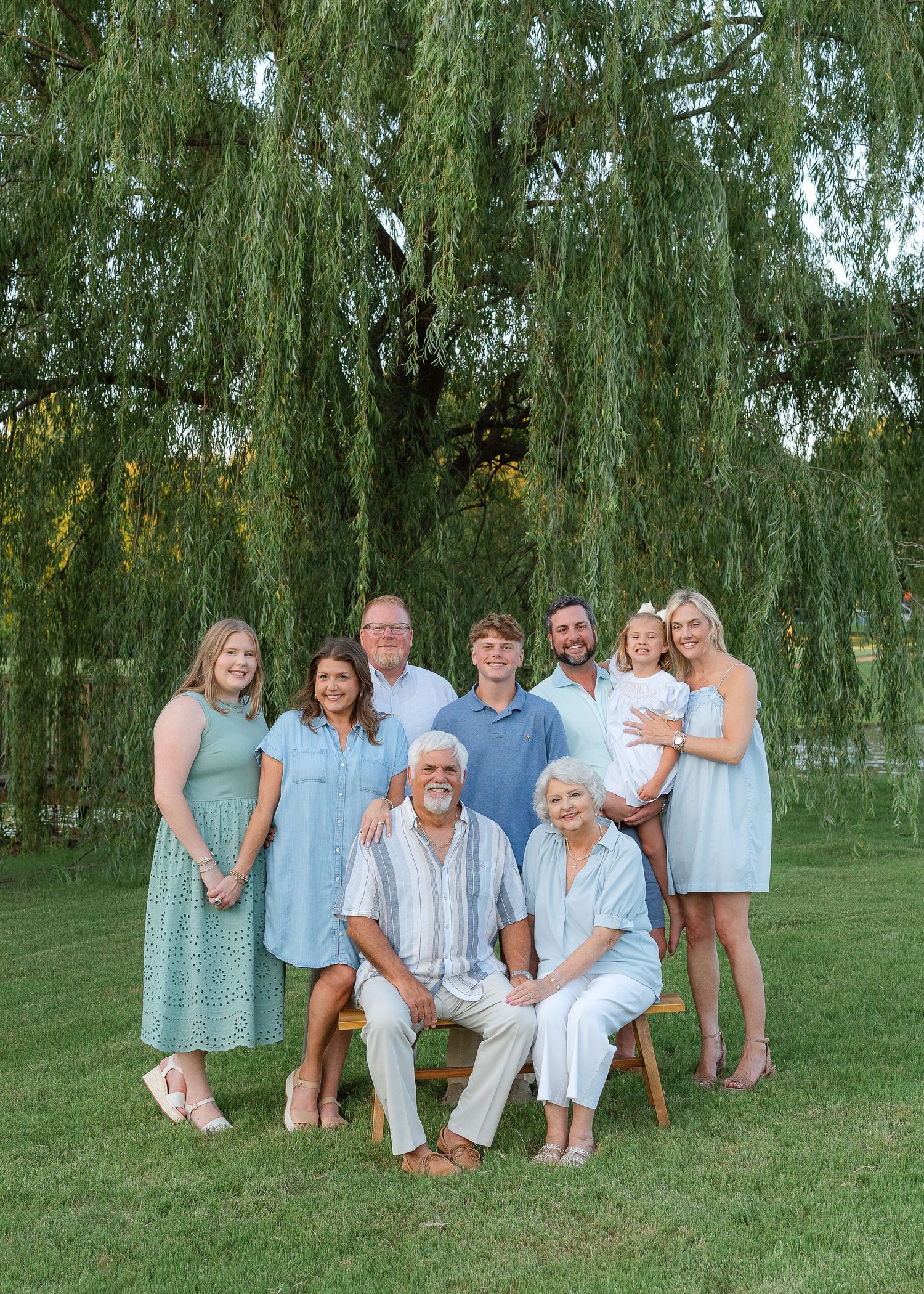 Multi-generational family portrait of nine people posing under weeping willow tree outdoors.