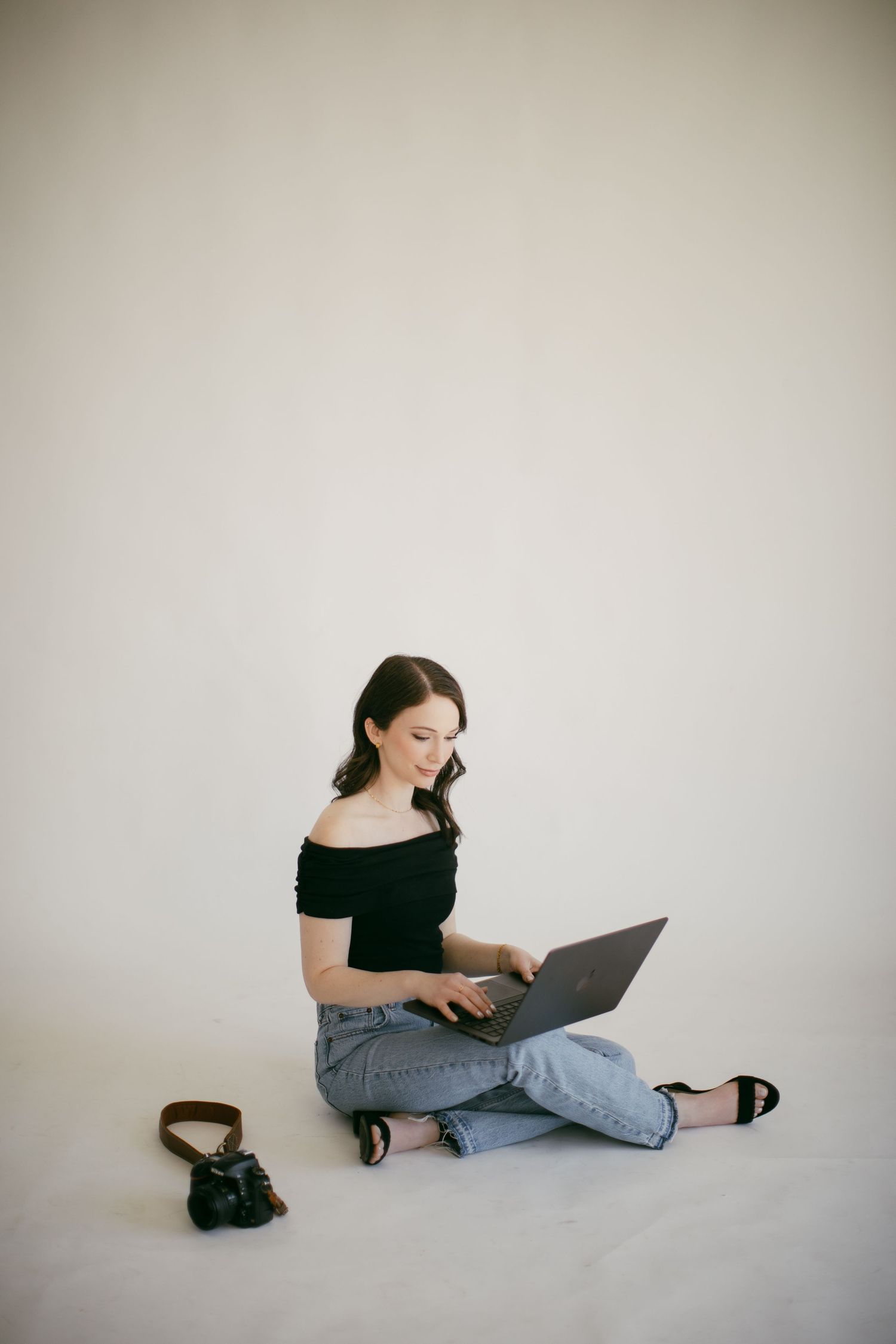 Young woman sitting cross-legged on floor smiling while working on a laptop computer.