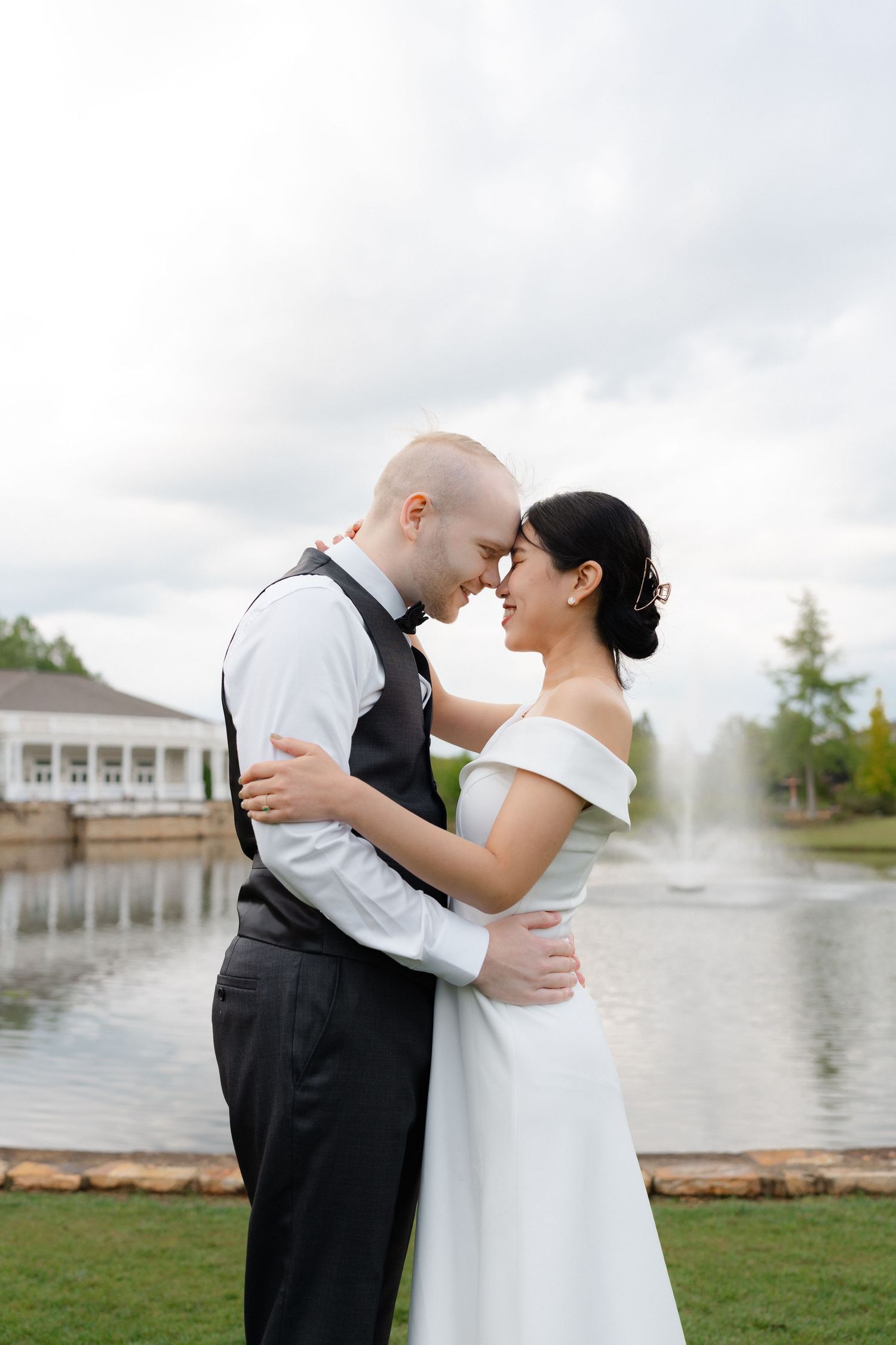 A bride and groom embrace near a fountain outdoors, sharing a romantic moment in wedding attire on their special day.