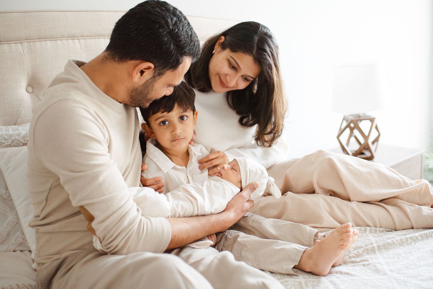 Loving family of three sitting together on a bed, admiring their newborn baby.