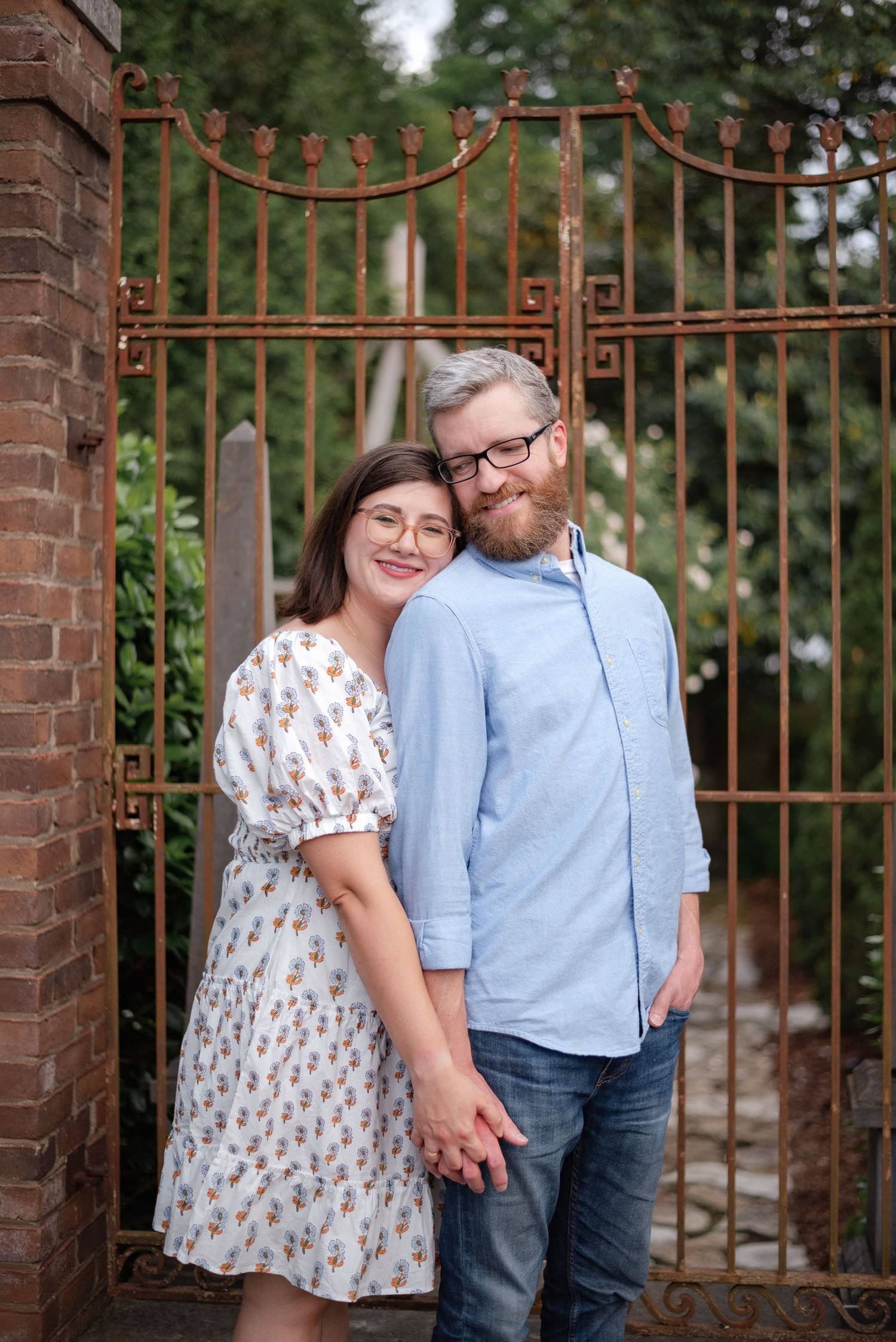Smiling couple holding hands in front of a rustic iron garden gate.