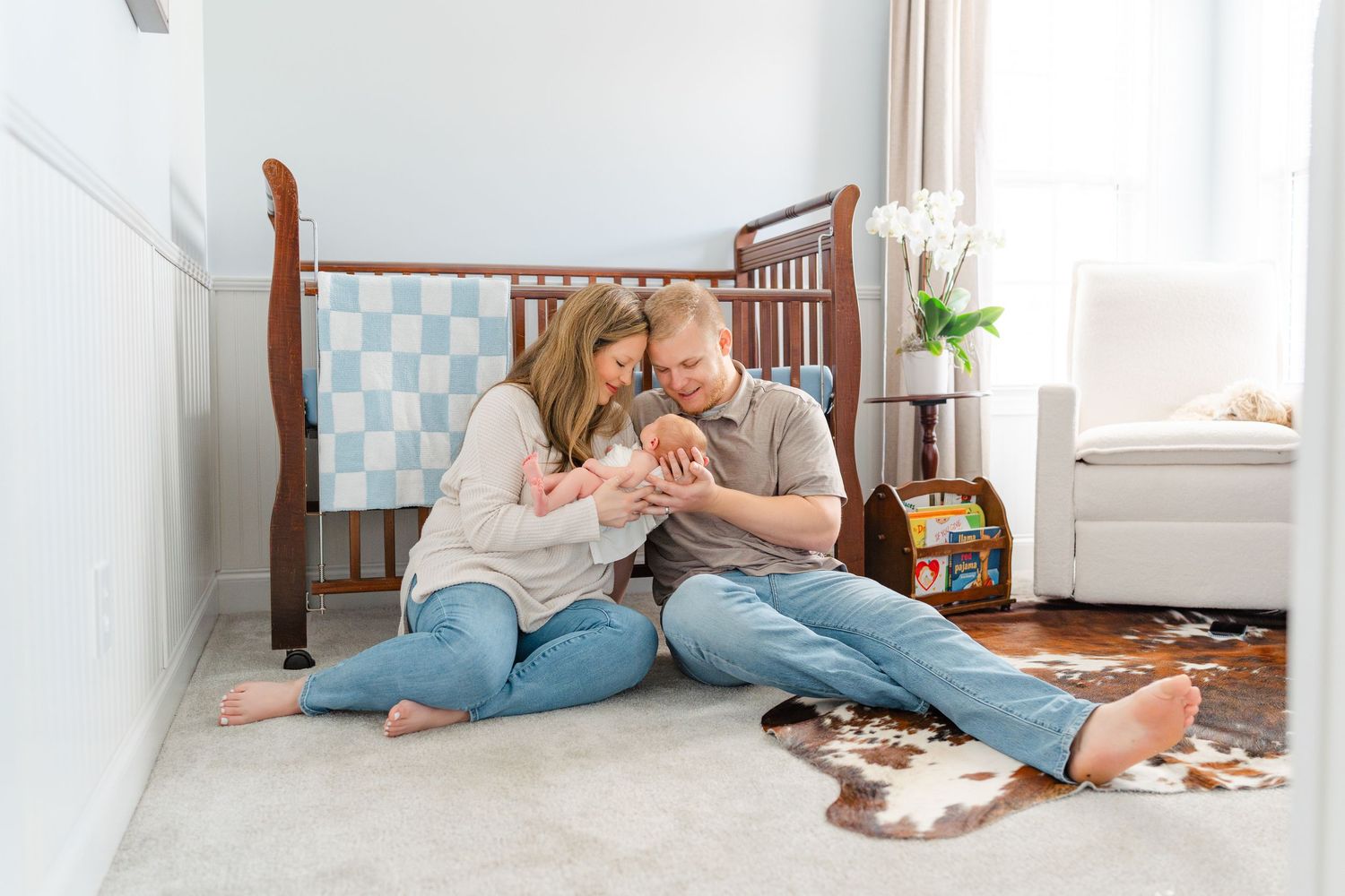 New parents sit on nursery floor together smiling and bonding with their newborn baby.