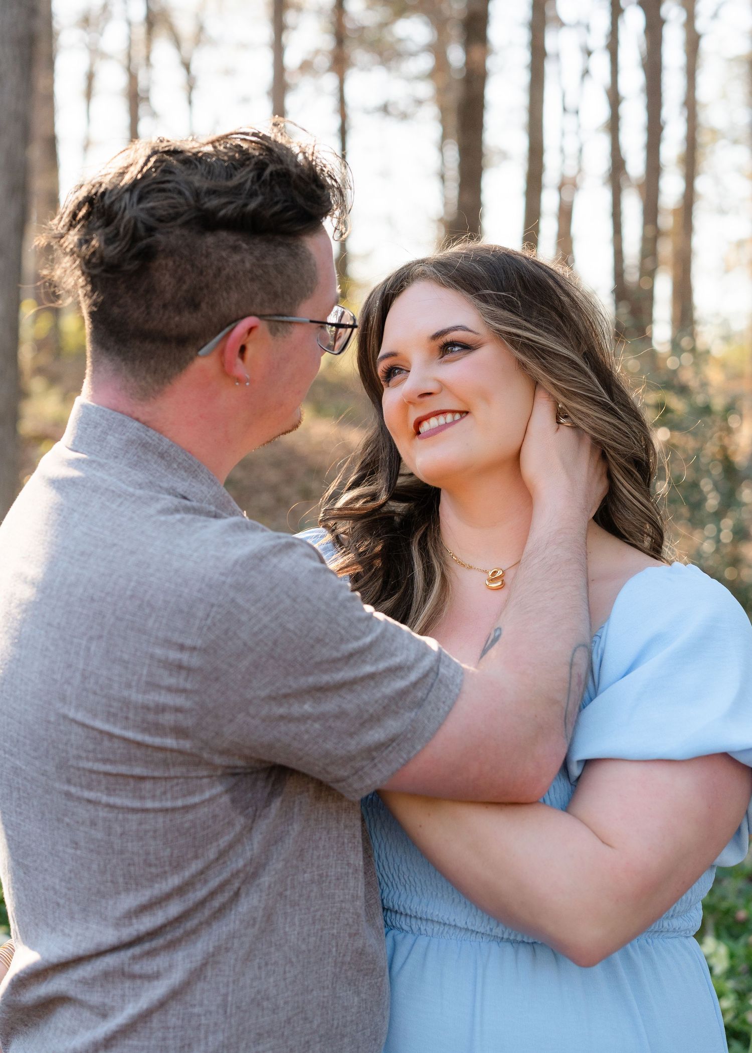 A man gently cups a smiling pregnant woman's face as they share a tender moment outdoors in golden light.