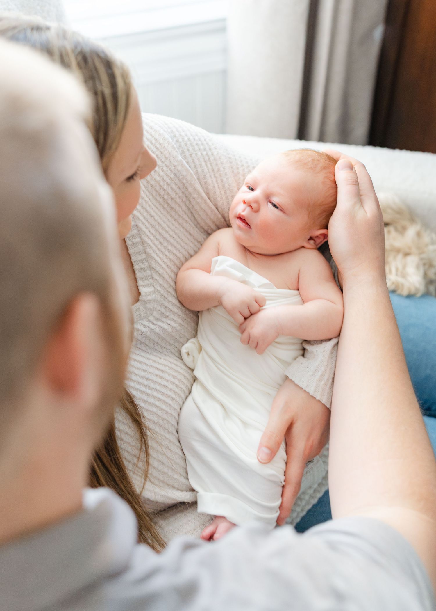 Parents gently cradle and admire their sleepy newborn baby wrapped in white cloth.