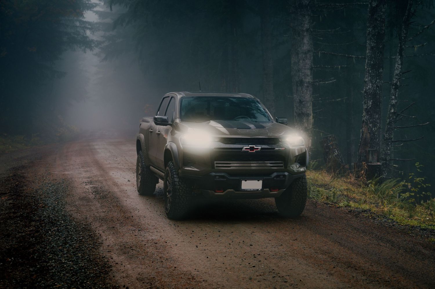 Black pickup truck with bright headlights on a foggy forest road at night.