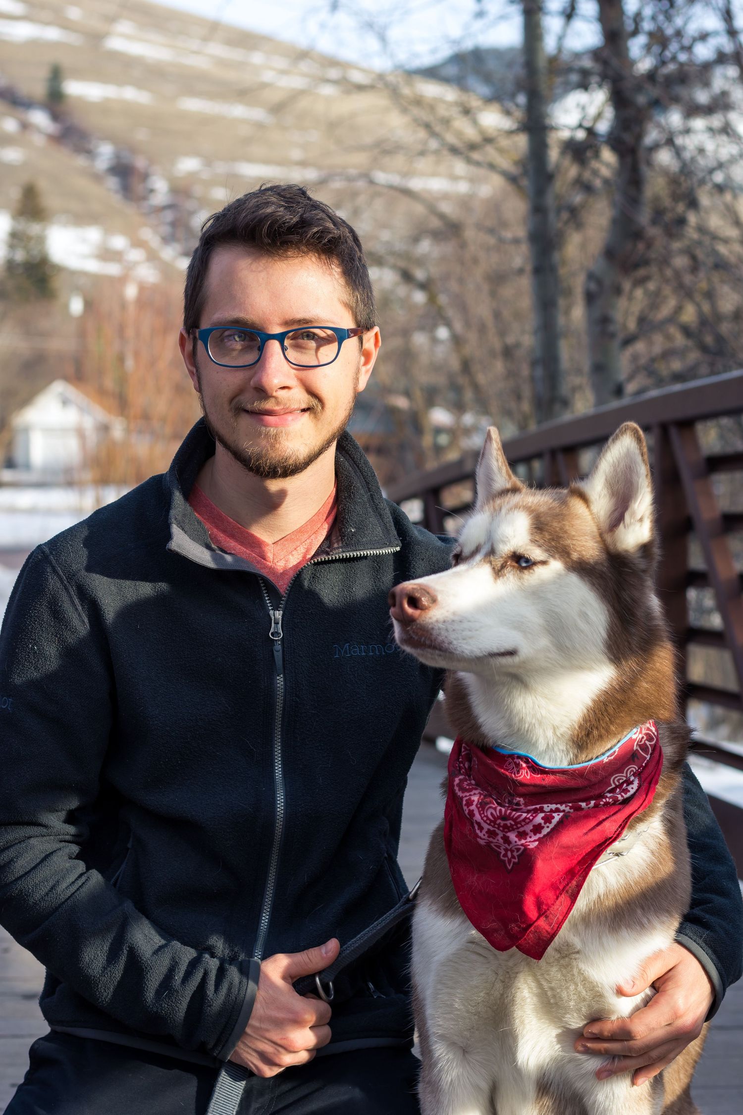 A person and their husky dog posing together on a snowy mountain bridge.
