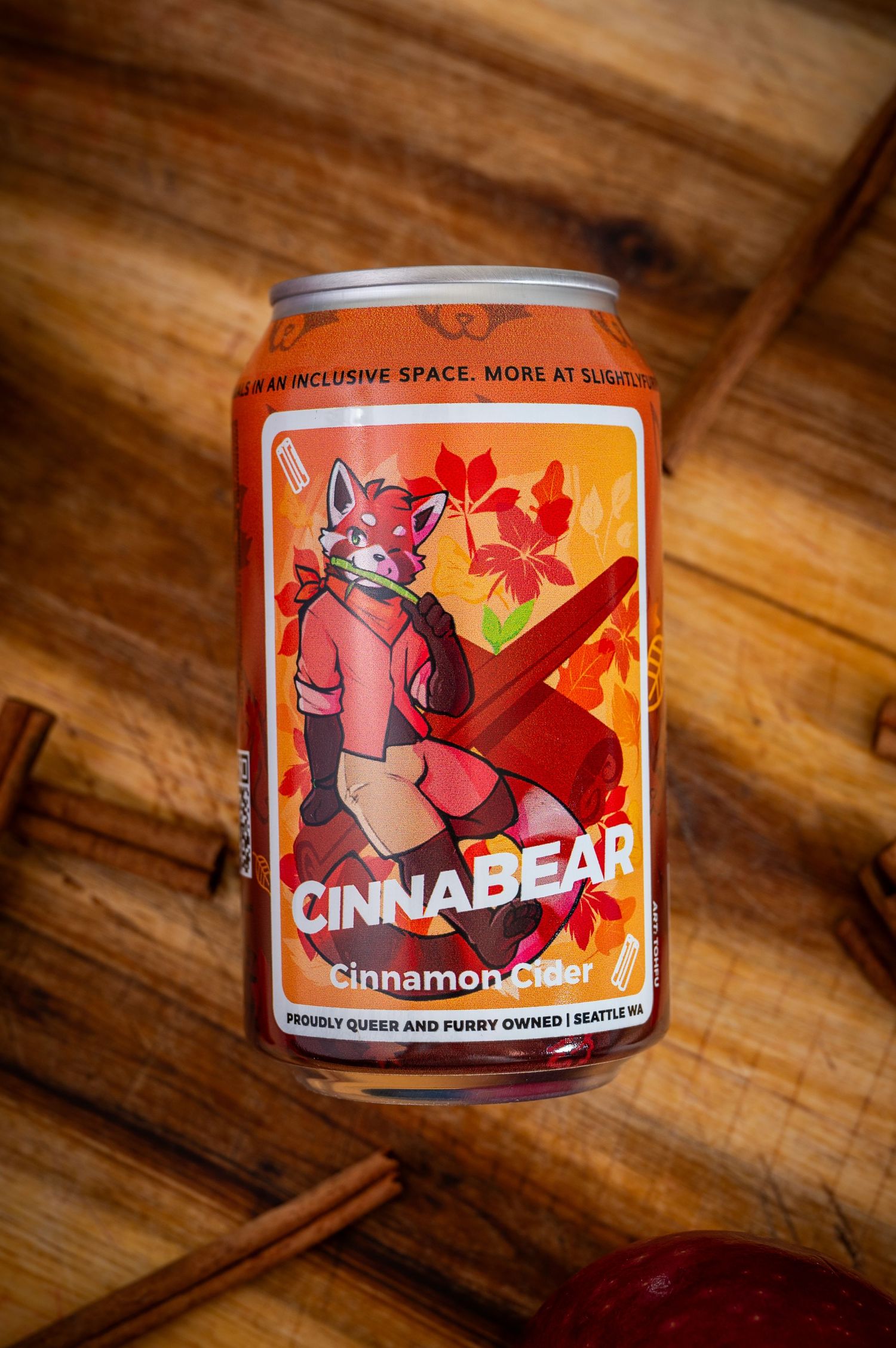 A can of Cinnabear cinnamon cider sits on a wooden surface with cinnamon sticks as a staged product photo.