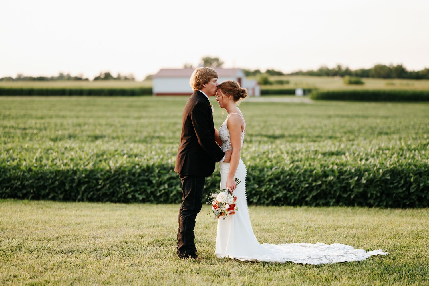 Newlyweds share an intimate moment on a green lawn during golden hour.