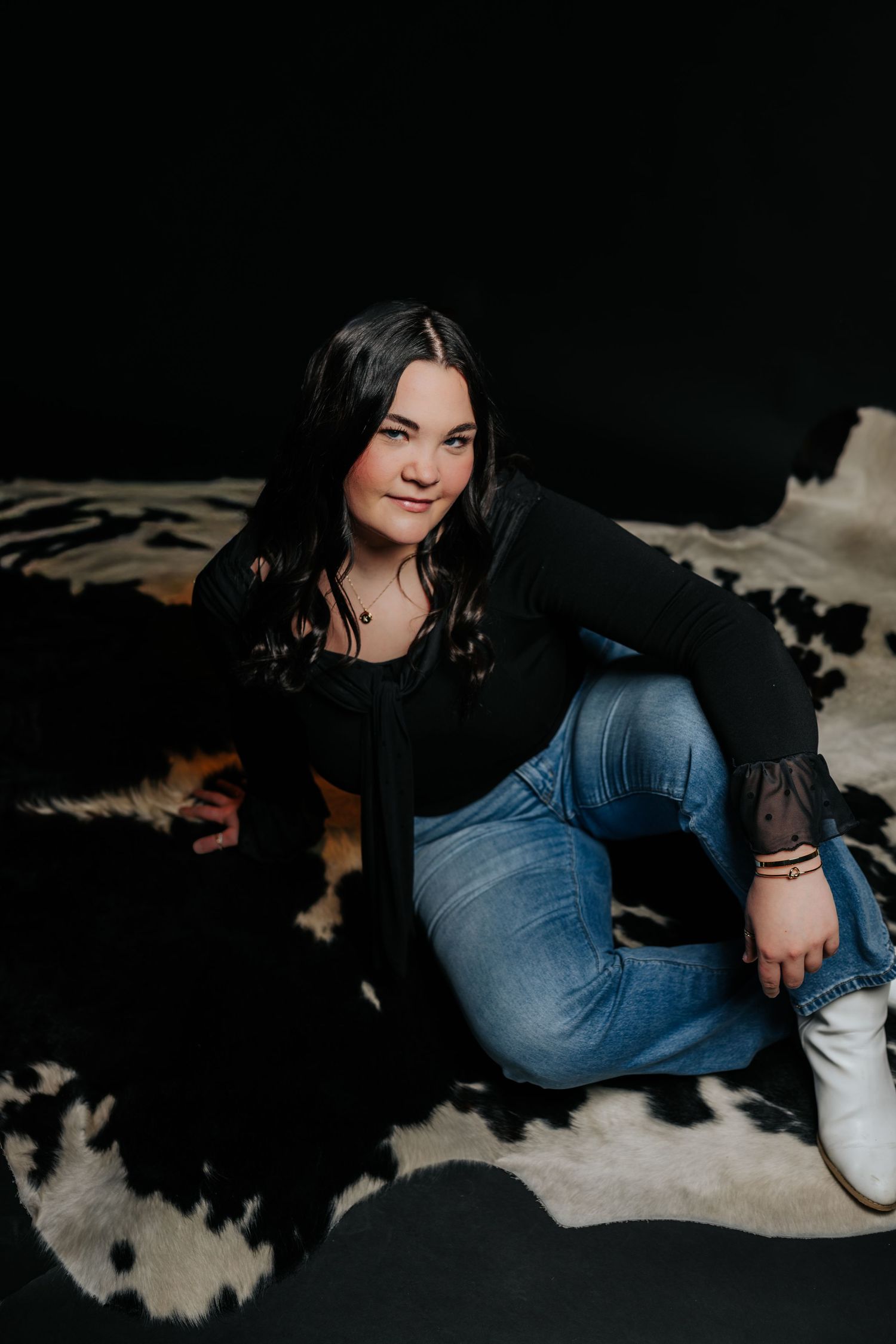 Artistic portrait series showing a person in dark clothing reclining on a black and white cowhide rug.