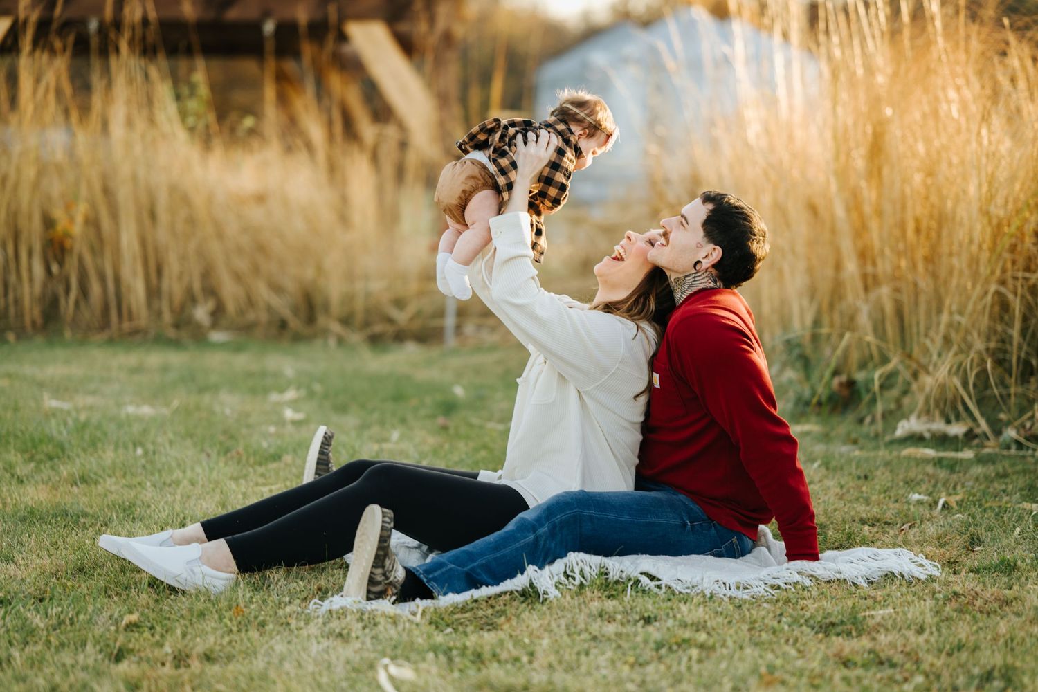 A couple in casual attire lies in golden grass during sunset, creating a romantic outdoor portrait.