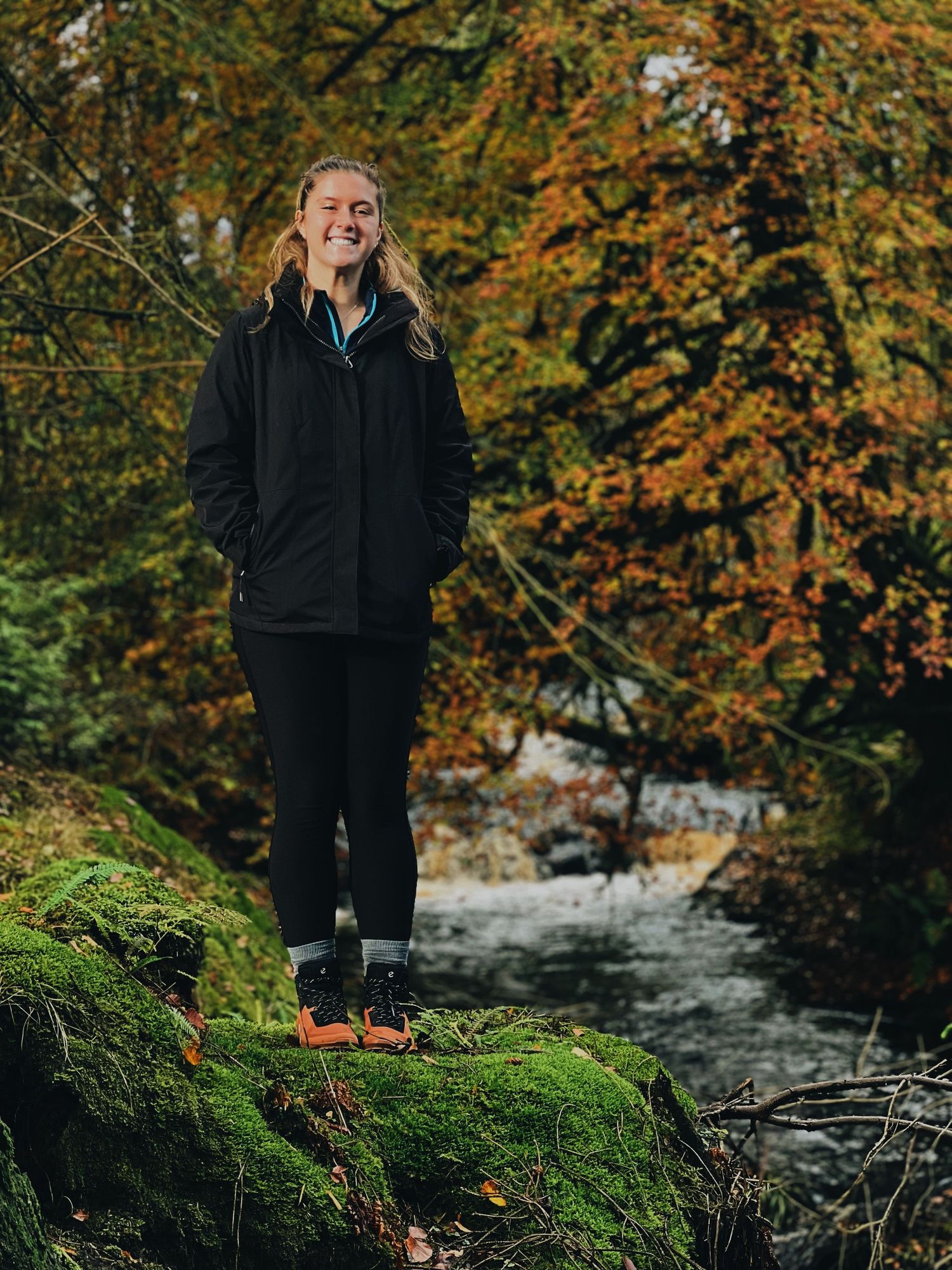 Outdoor portrait session near a mossy creek with autumn foliage in the background.