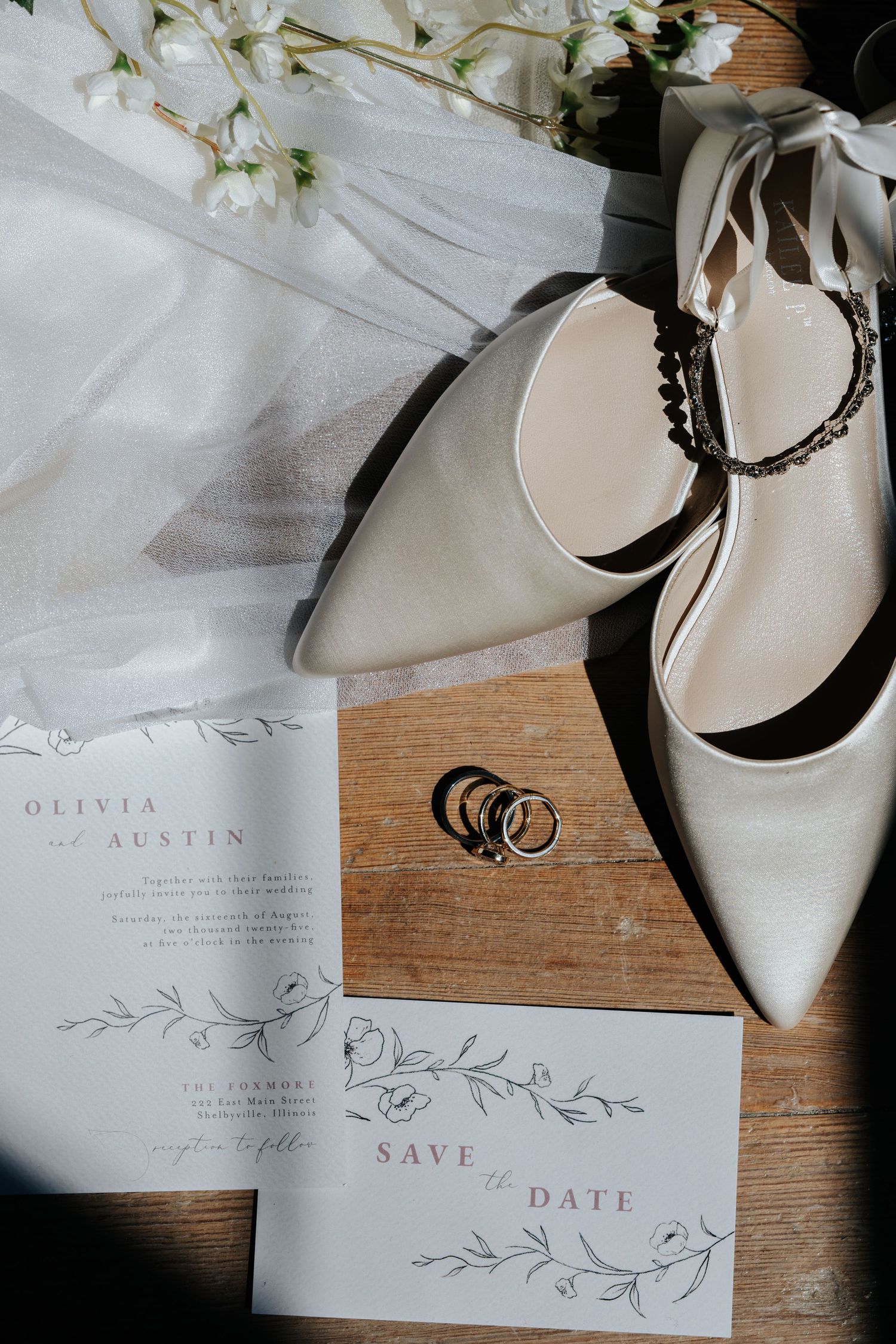 Elegant white wedding stationery with floral designs and white shoes arranged on a wooden surface with delicate flowers.