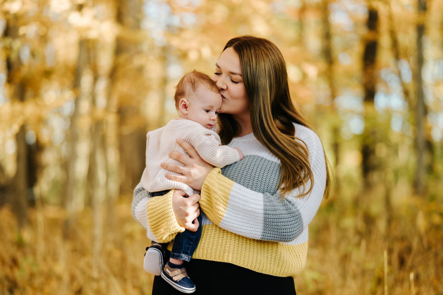 A tender moment between parent and child surrounded by golden autumn foliage in a forest setting.