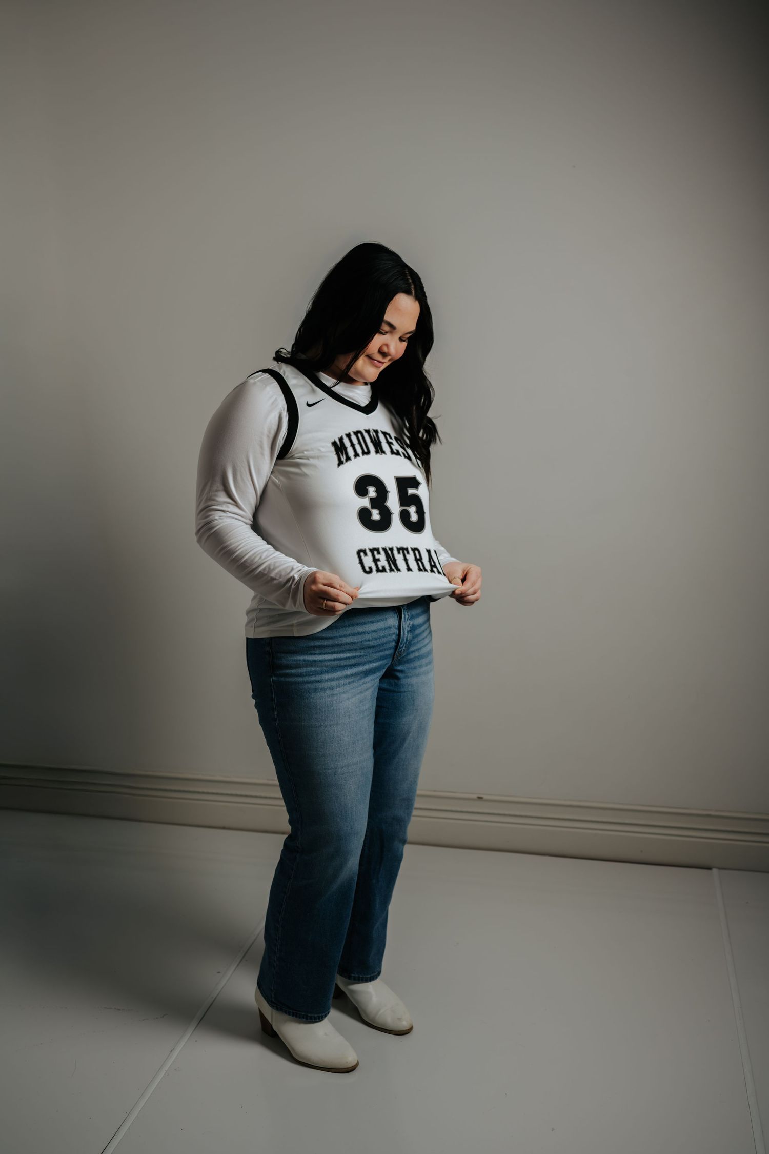 Person wearing a gray numbered jersey and jeans poses against a light colored wall.