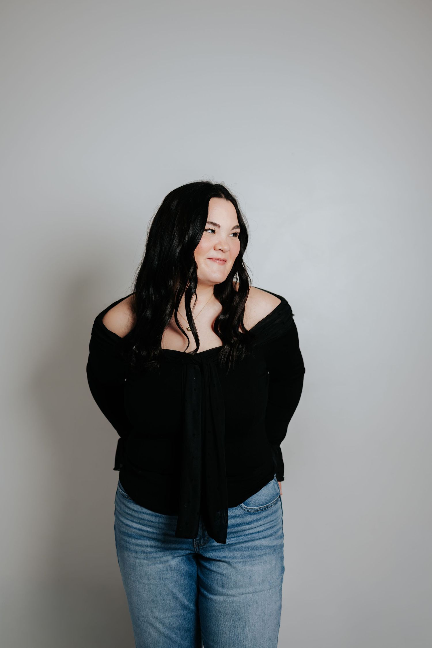 Portrait against grey background wearing black top and blue jeans showing casual style.