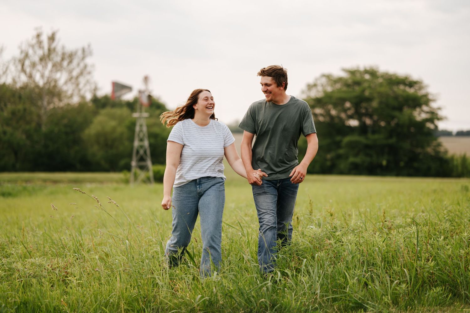 Playful couple walking through a green field on a cloudy day.