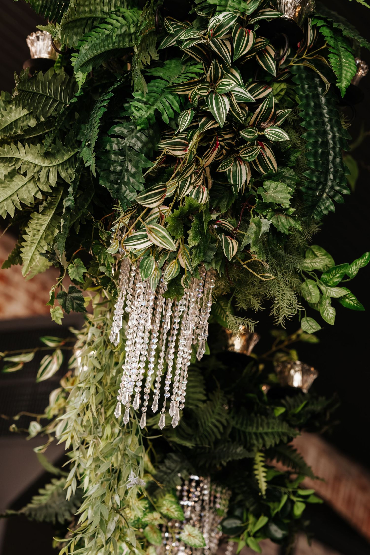 Crystal chandelier decorations hanging elegantly among lush green foliage and ferns.