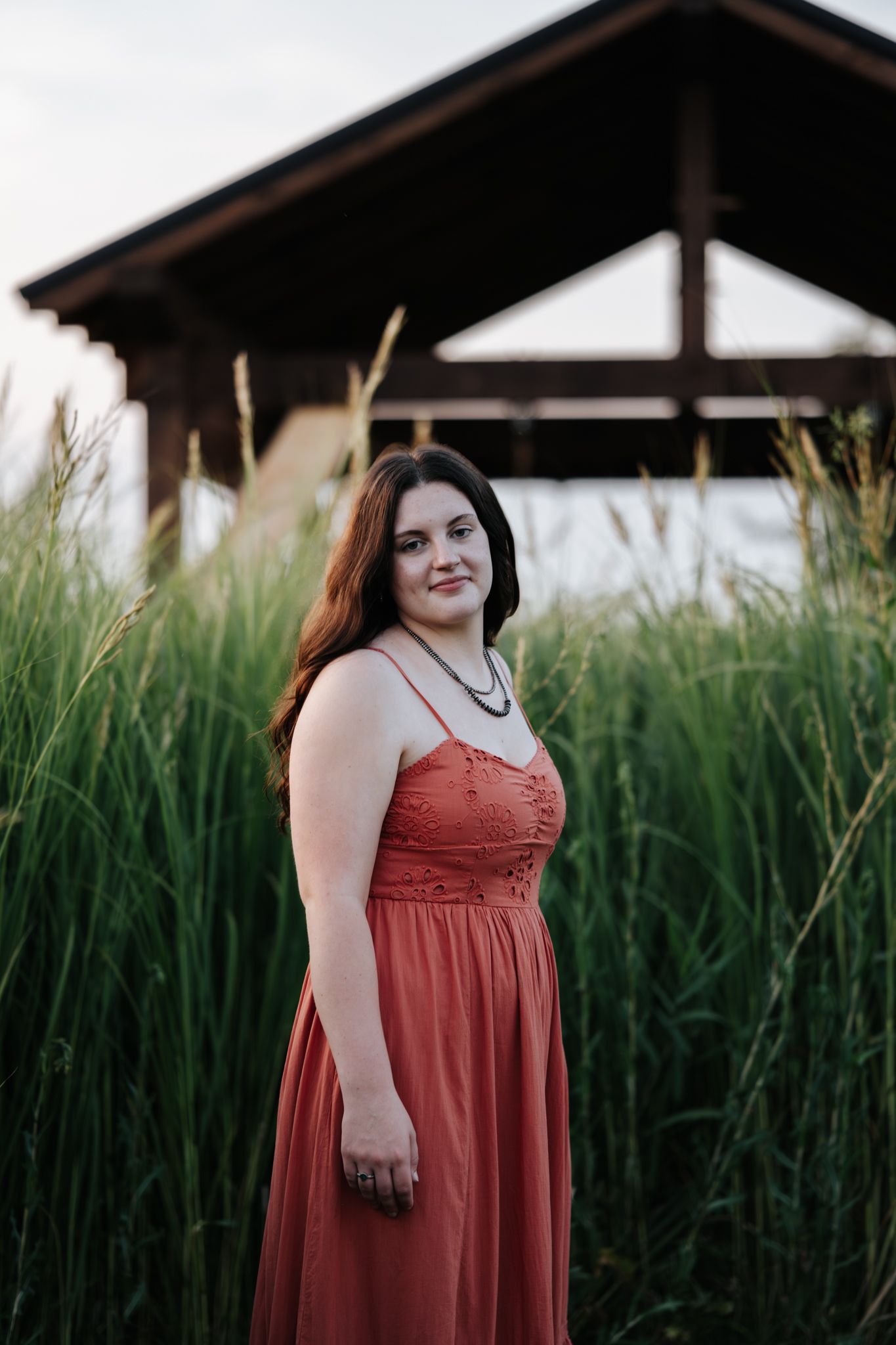 A coral-colored dress stands out against tall green grass in an outdoor portrait session.