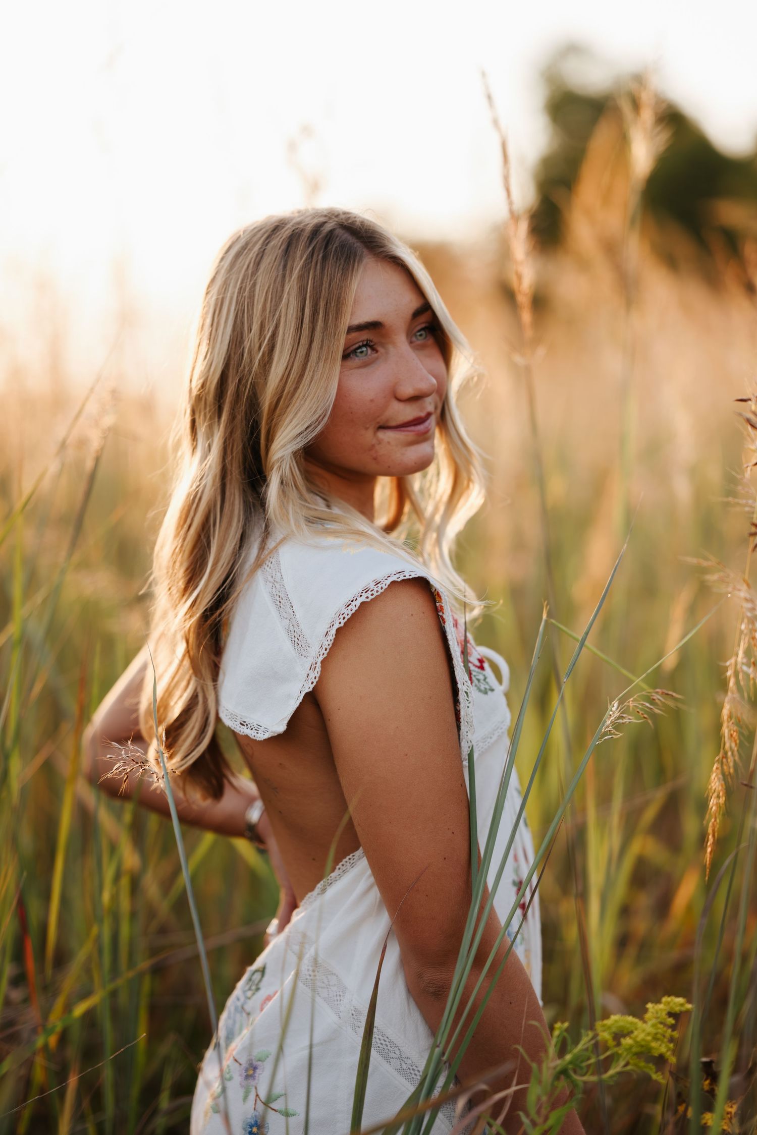 Woman in white dress poses gracefully among tall grass during golden hour.