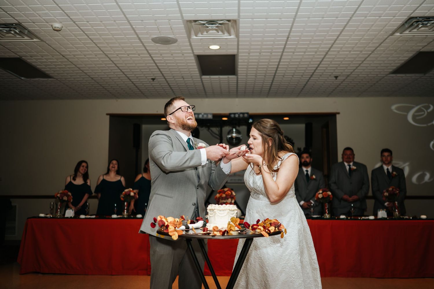Wedding reception in a banquet hall with decorative lighting and red tablecloths.