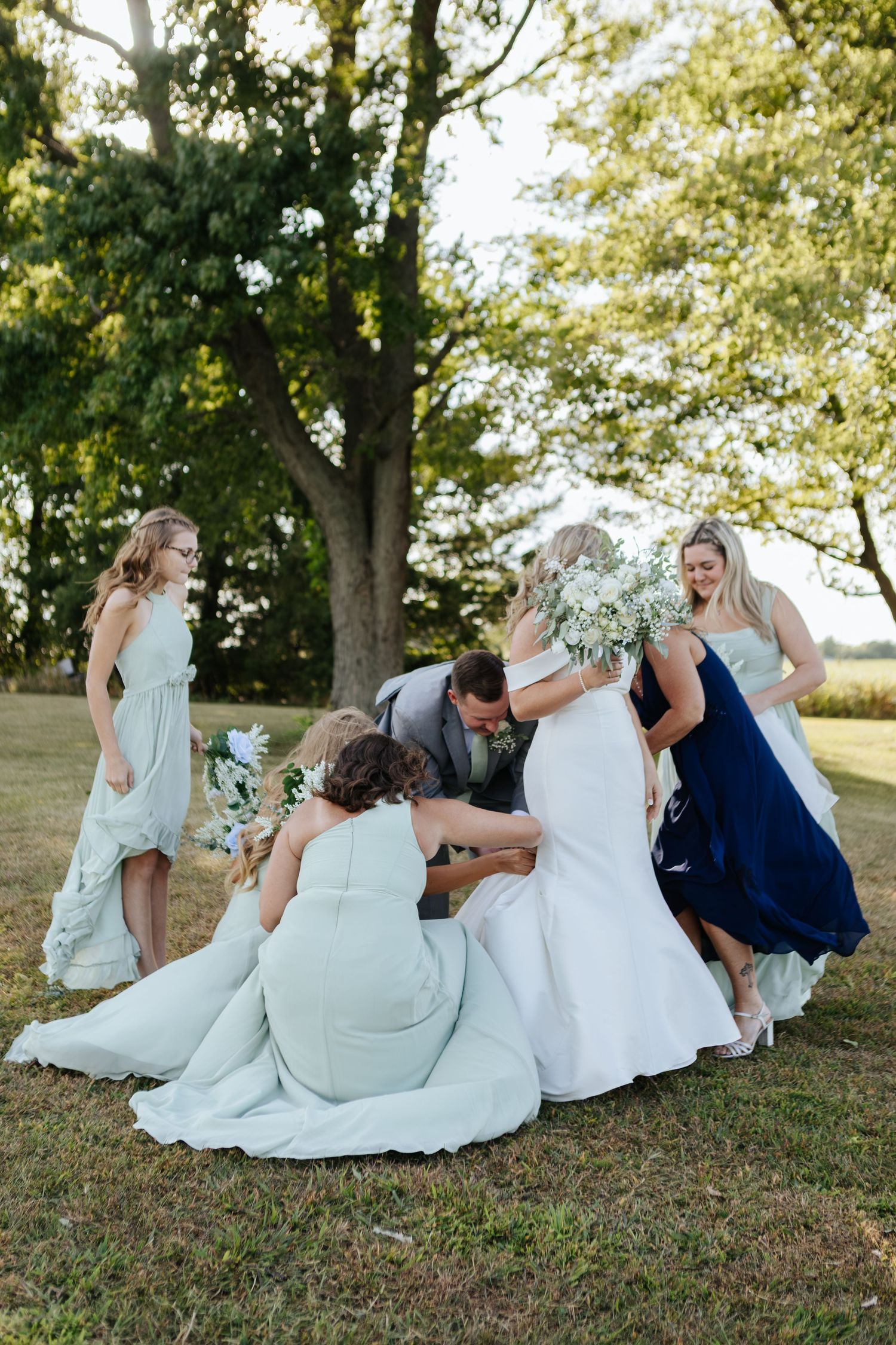 Wedding party lounging on grassy hill in mint green dresses and formal attire.