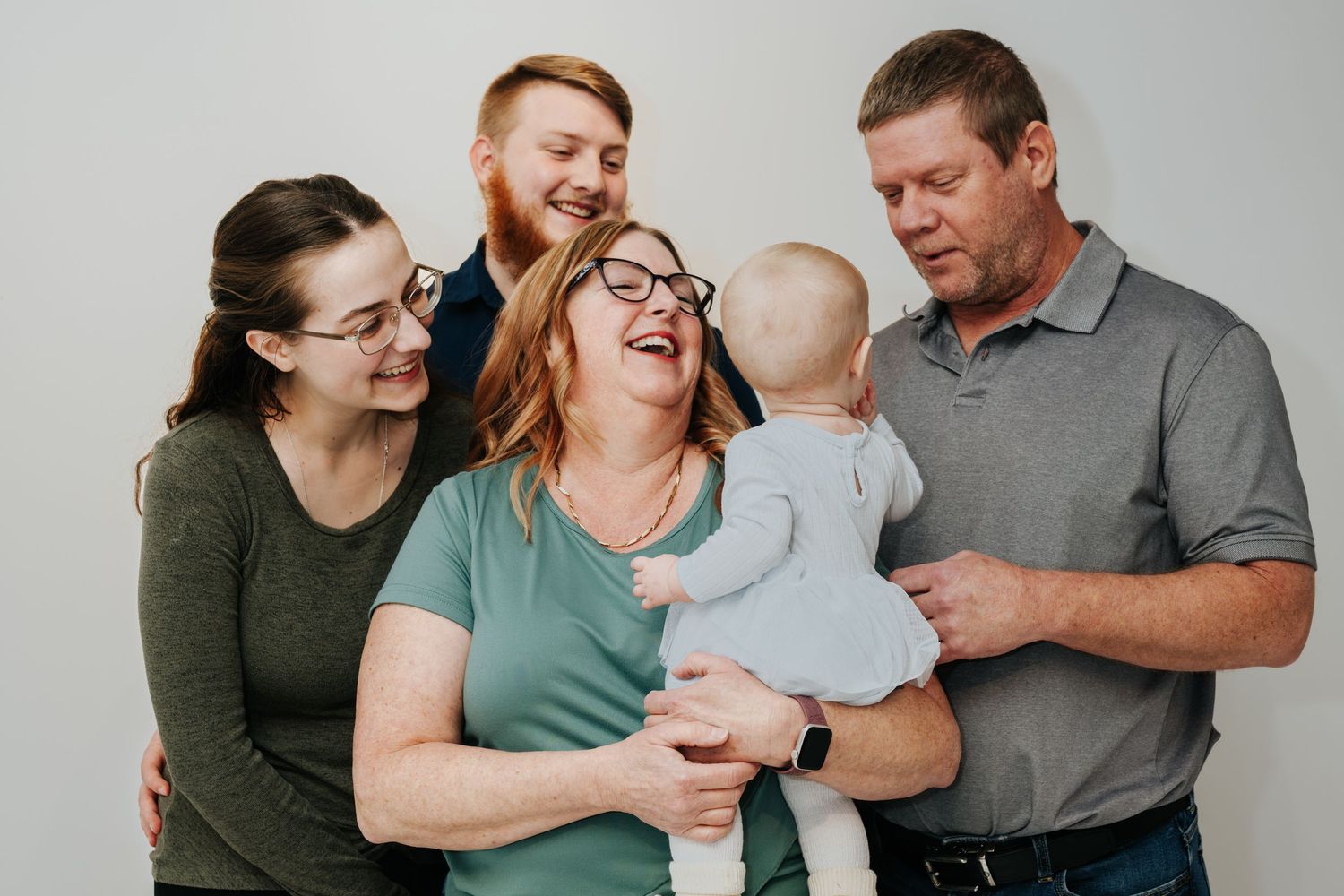 A family portrait session against a neutral grey background showing warm expressions.