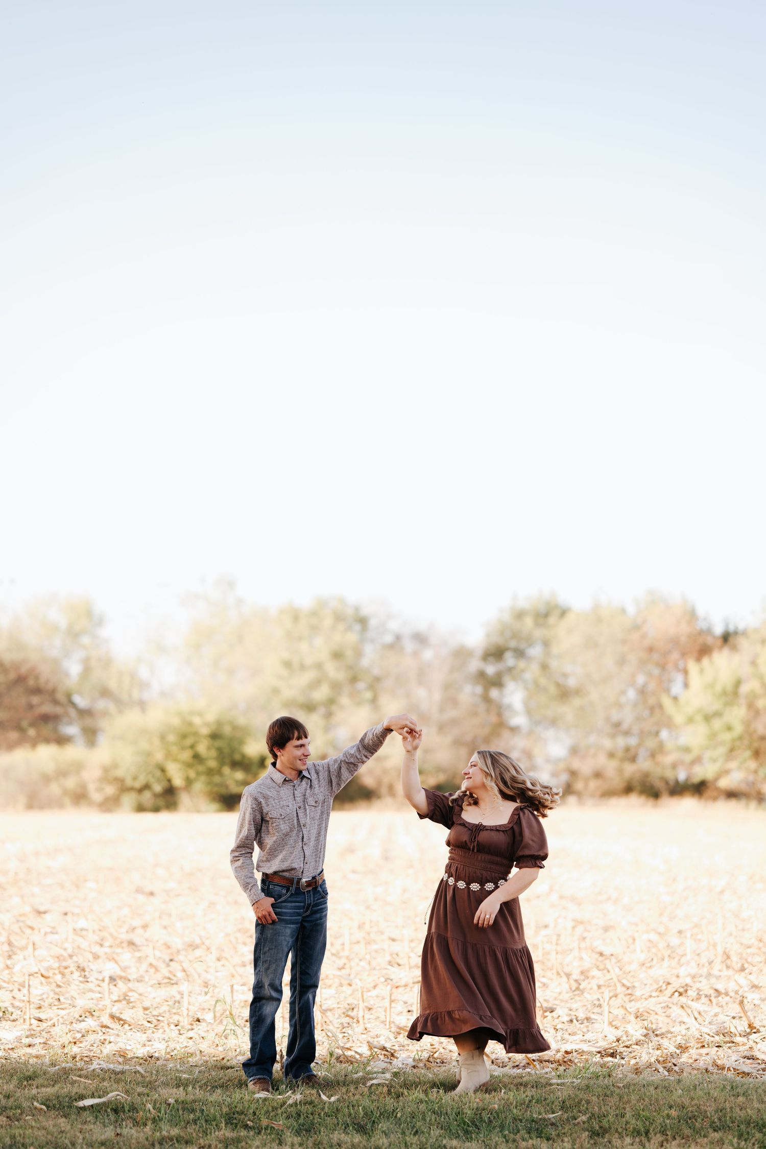 Couple dancing and twirling in sunlit field during golden hour photoshoot.