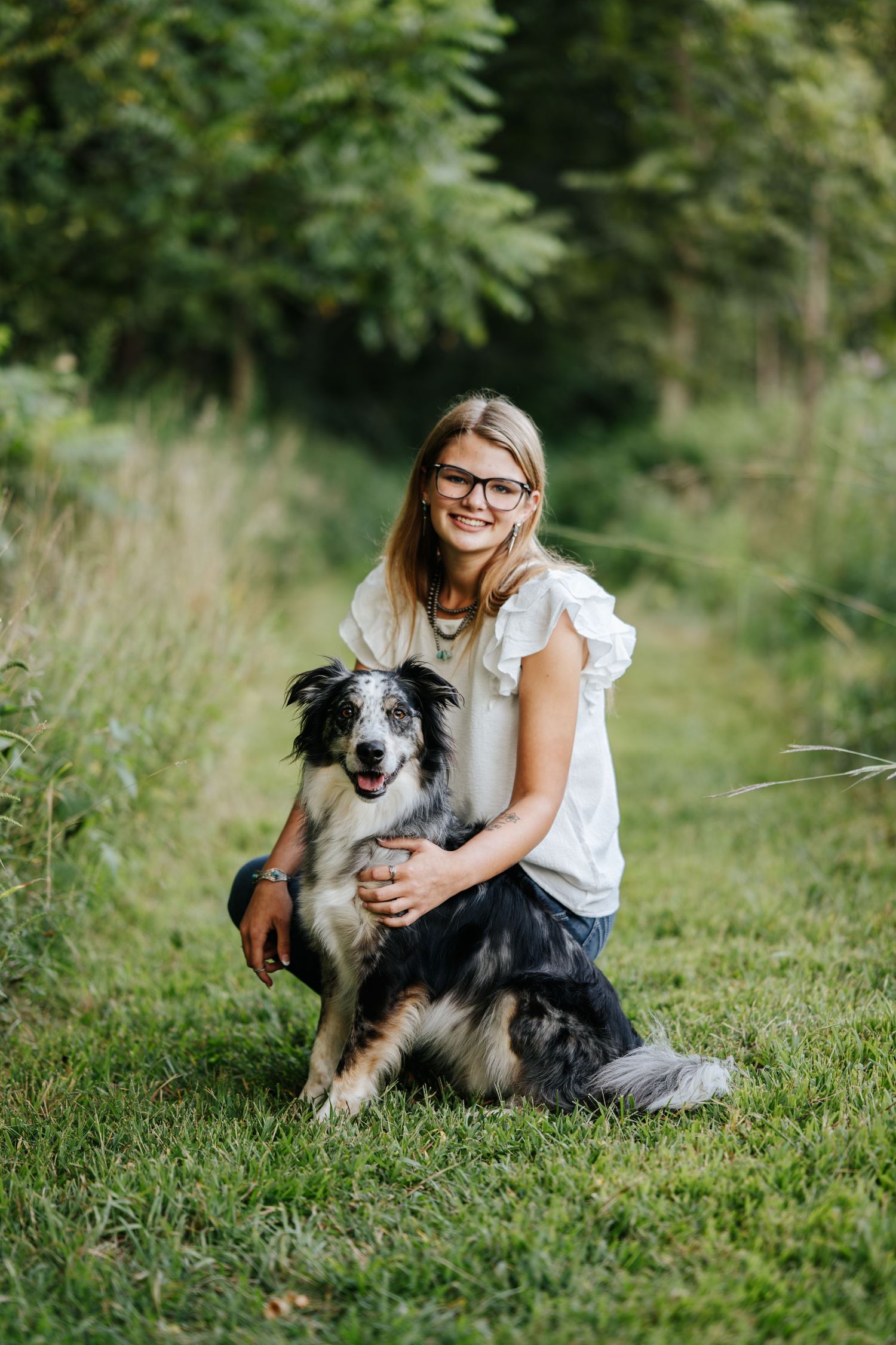 Person in white top sits with a black and white border collie dog in a grassy field.