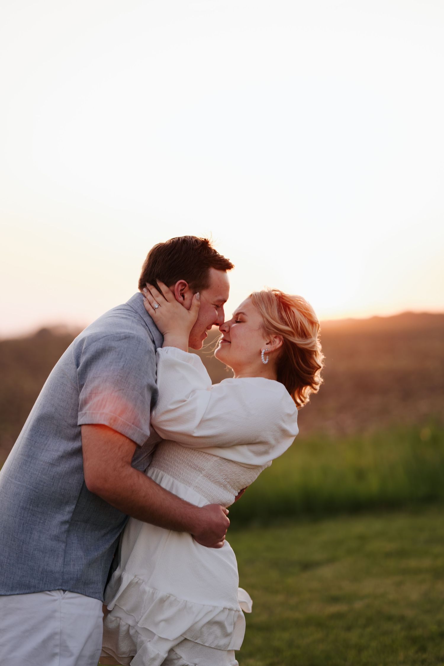Romantic couple embracing and kissing in golden sunset light on grassy field.