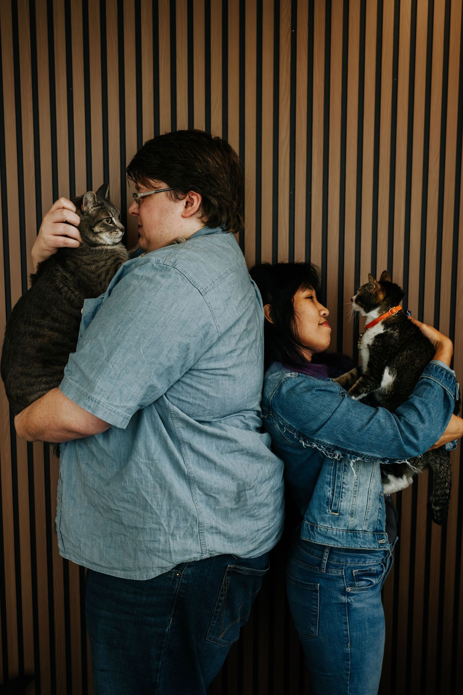 A couple embraces in front of a wooden slatted wall during an intimate photoshoot.