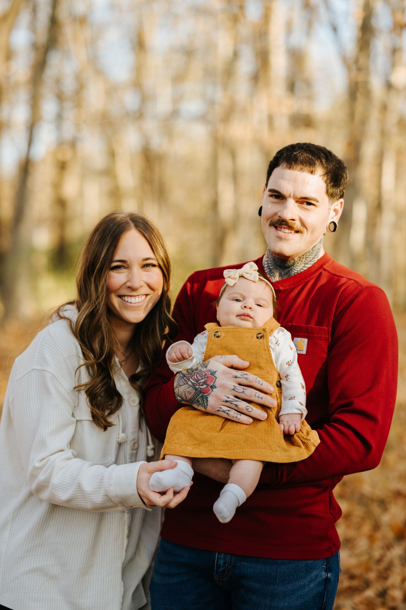Family enjoying autumn photo session in wooded area wearing red and white outfits in natural light.