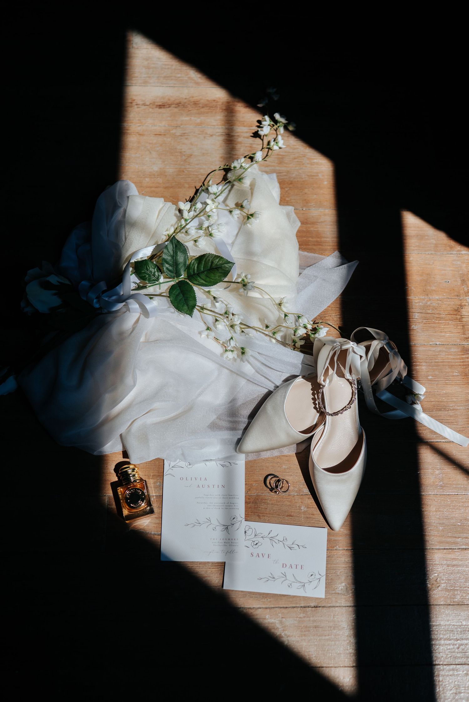 Wedding stationery and white flowers arranged in dramatic window light on wooden surface.